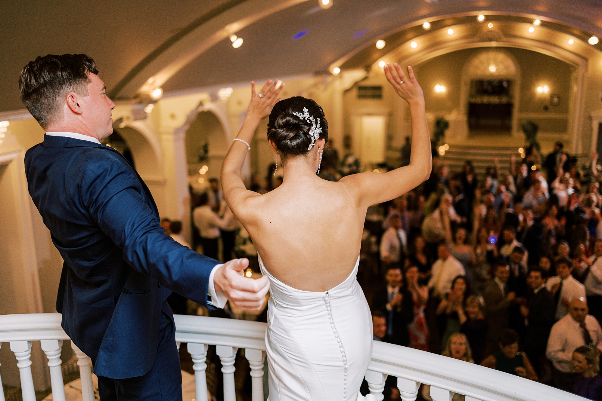 bride waves at guests from balcony with groom in club