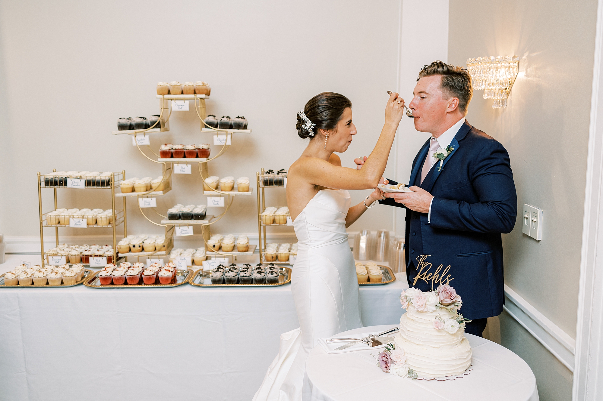bride feeds groom wedding cake in front of cupcake display in Philly PA