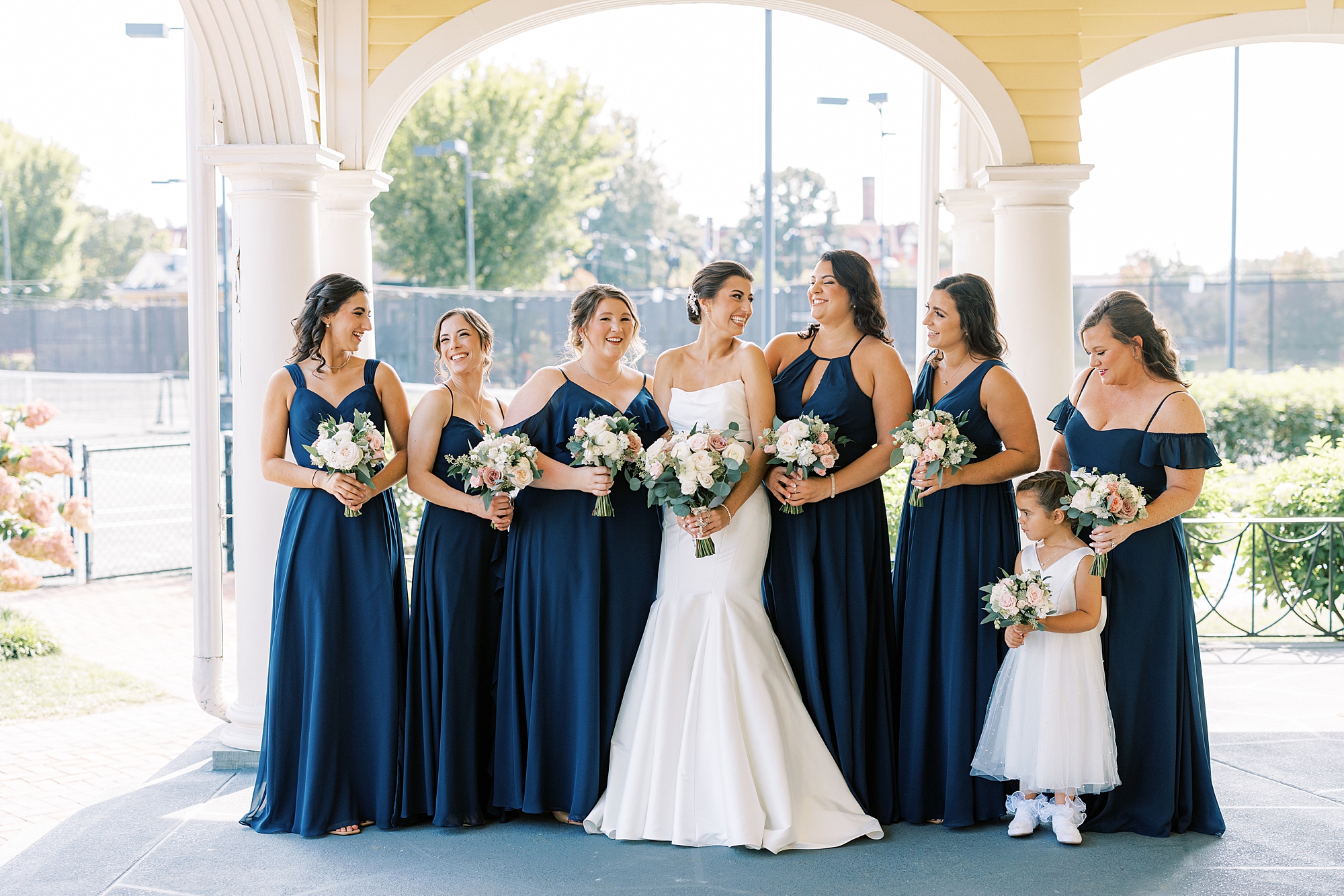 bride smiles at bridesmaids in navy gowns with pastel flowers in Philadelphia PA