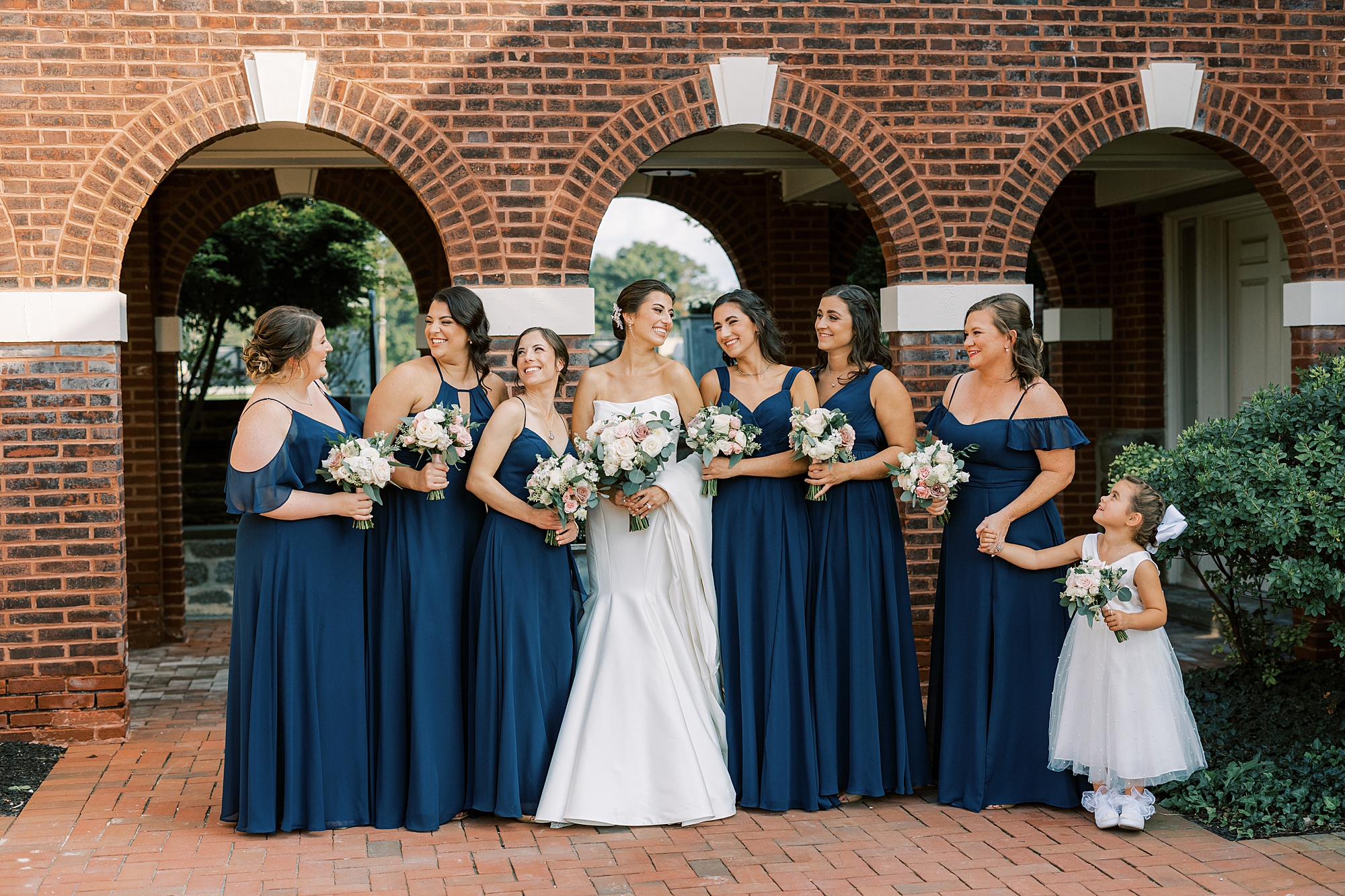 bride smiles at bridesmaids in navy gown with flower girl outside the Philadelphia Cricket Club