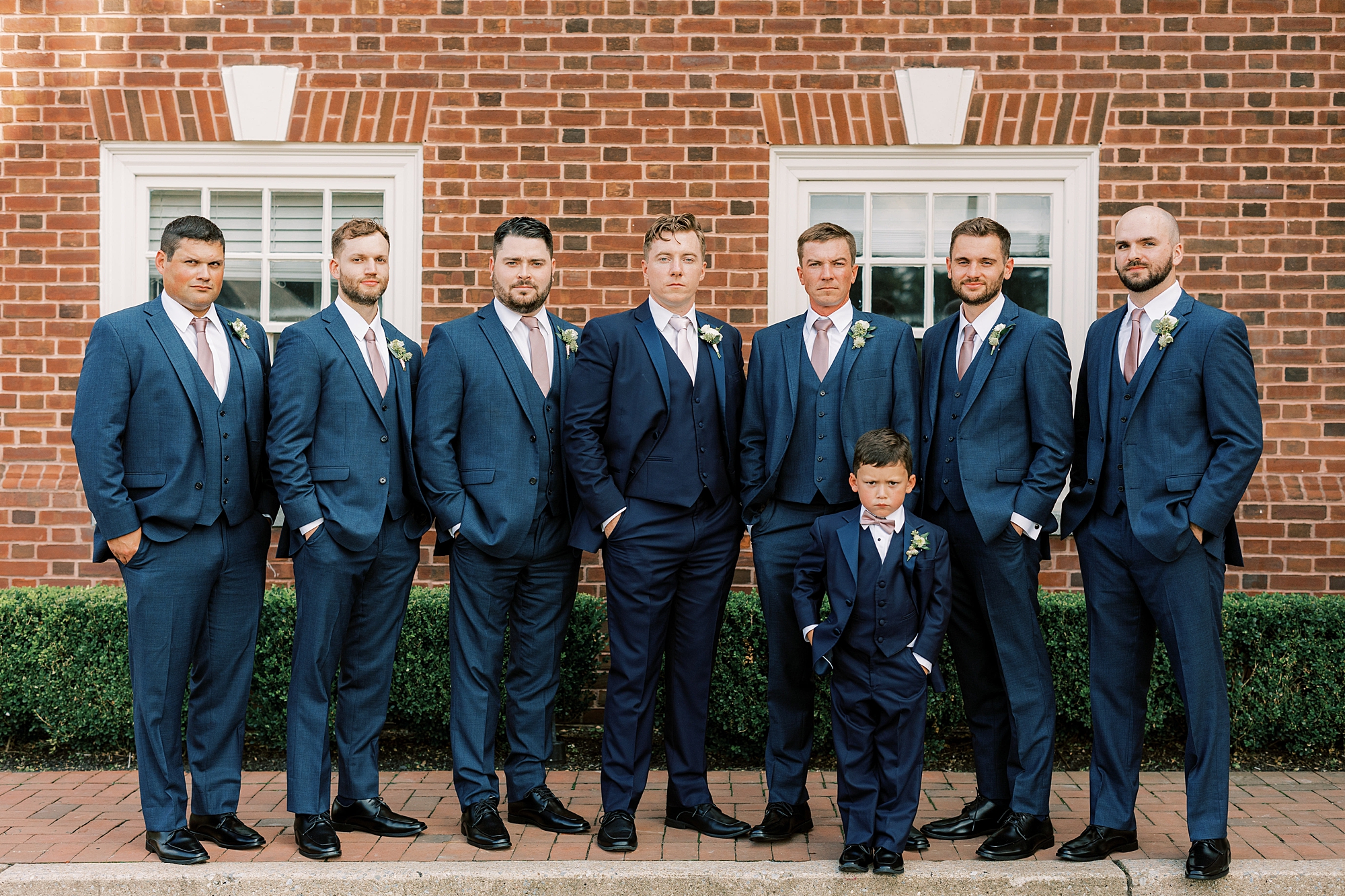 groom stands with groomsmen in navy suits with hands in pocket 