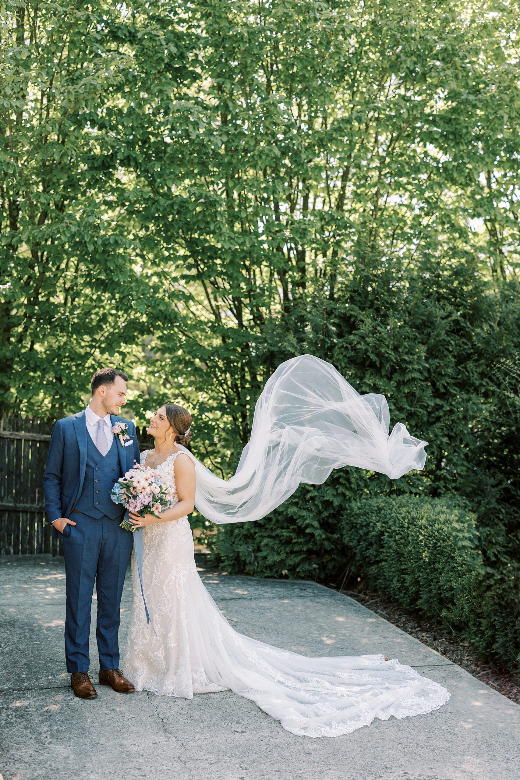 bride and groom smile together while bride's veil floats behind them