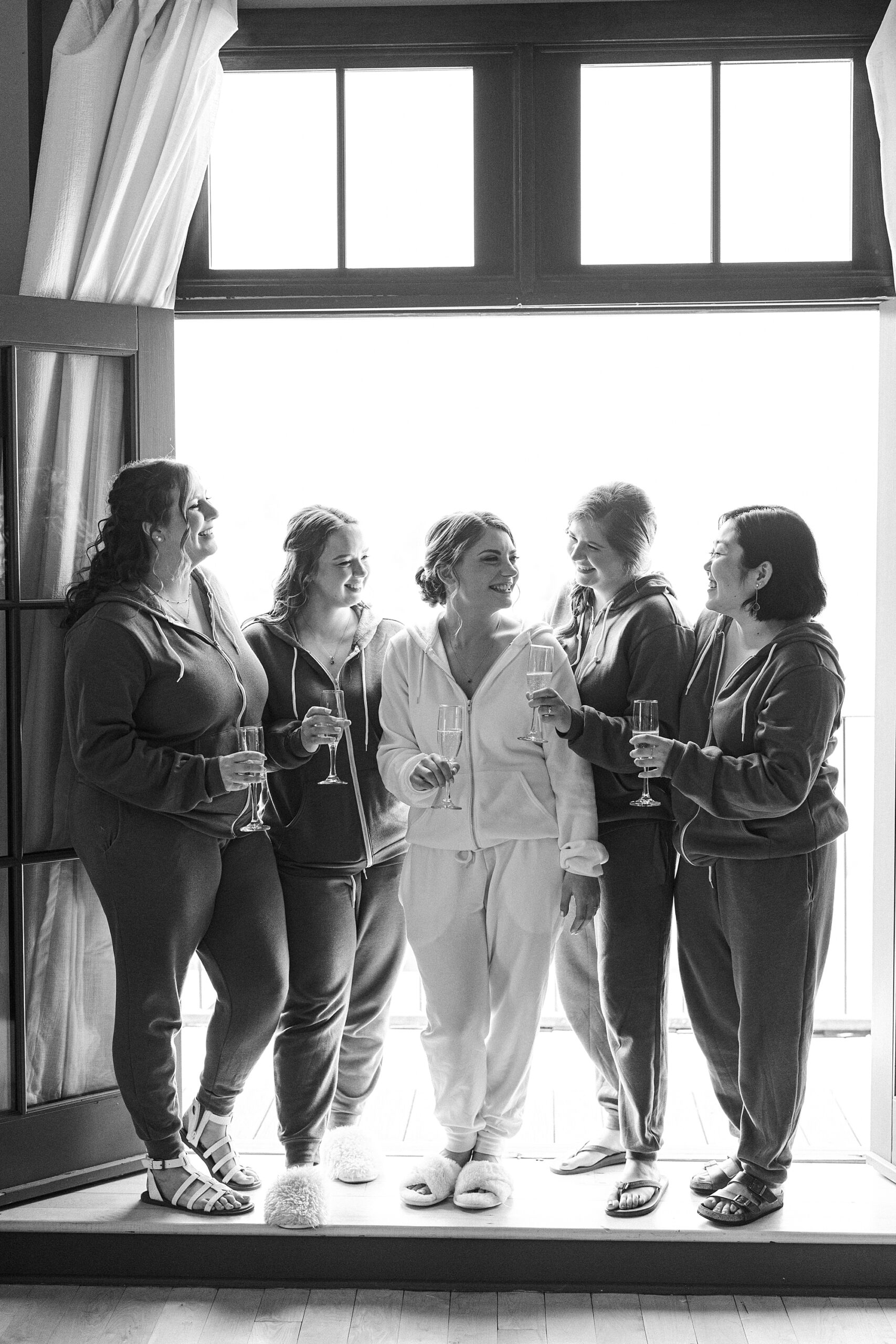 bridesmaids pose with bride in window at Lake House Inn holding champagne 