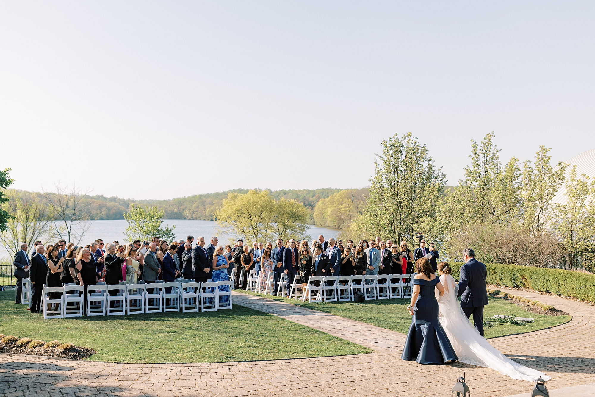 bride and parents walk to aisle for ceremony in the gardens at Lake House Inn with pink and purple flower installation