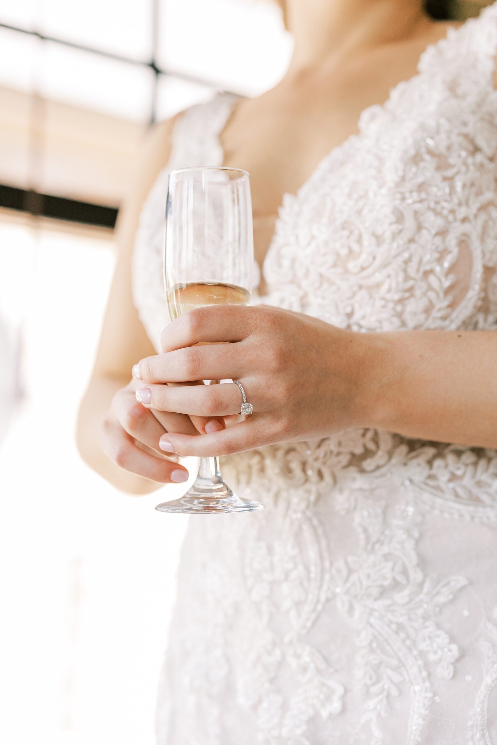 bride holds glass of champagne in front of lace details on wedding dress