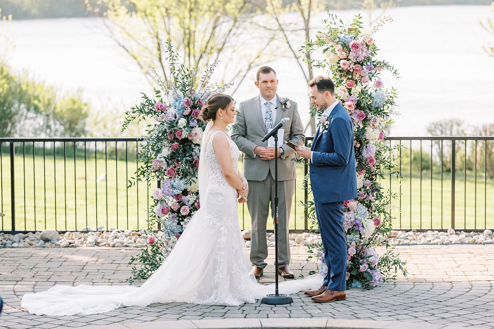 groom reads vows to bride during ceremony in the gardens at Lake House Inn with pink and purple flower installation