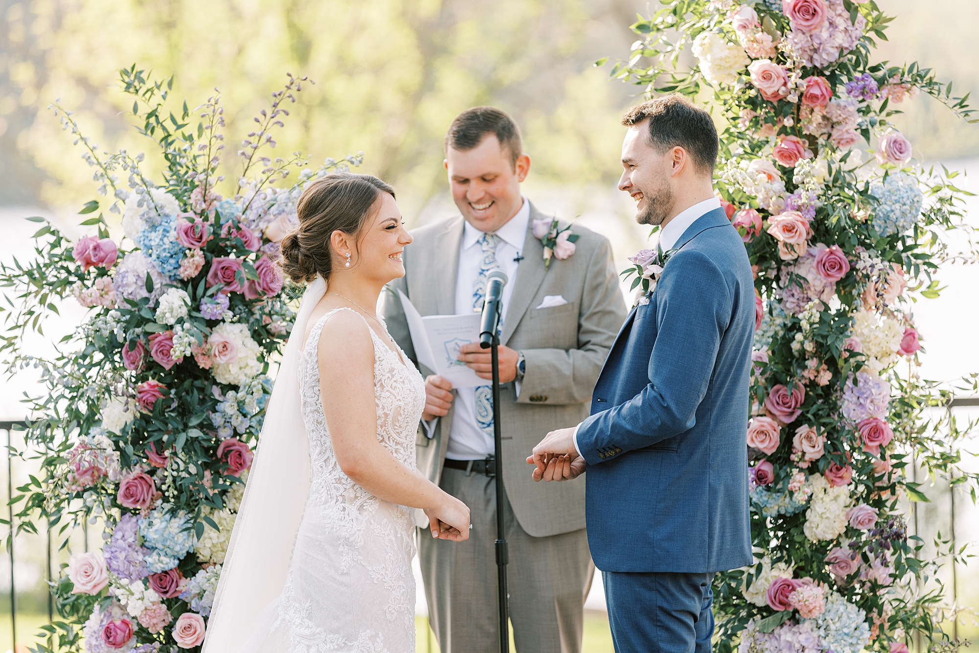 bride and groom exchange vows during ceremony in the gardens at Lake House Inn with pink and purple flower installation