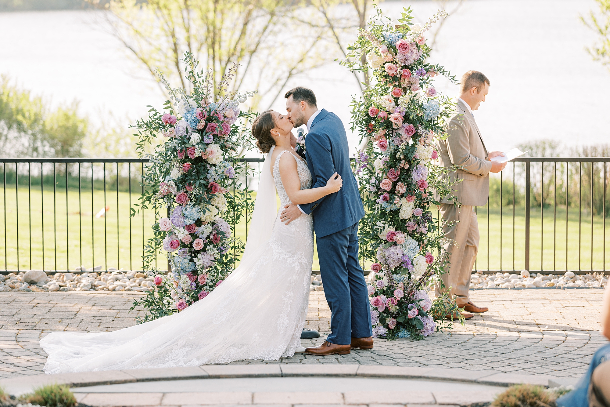 newlyweds kiss during ceremony in the gardens at Lake House Inn with pink and purple flower installation