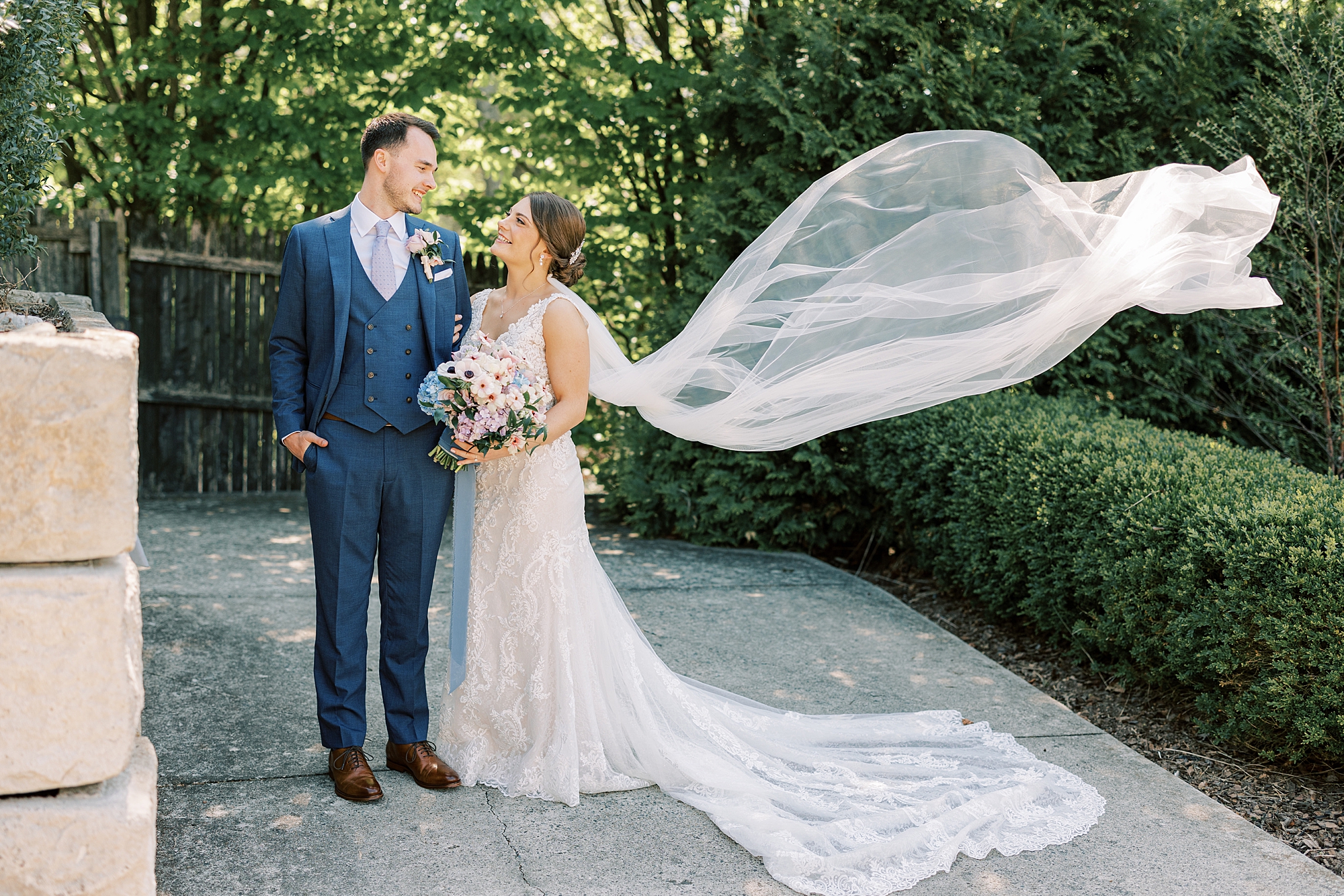 newlyweds smile together while bride's veil floats behind them 