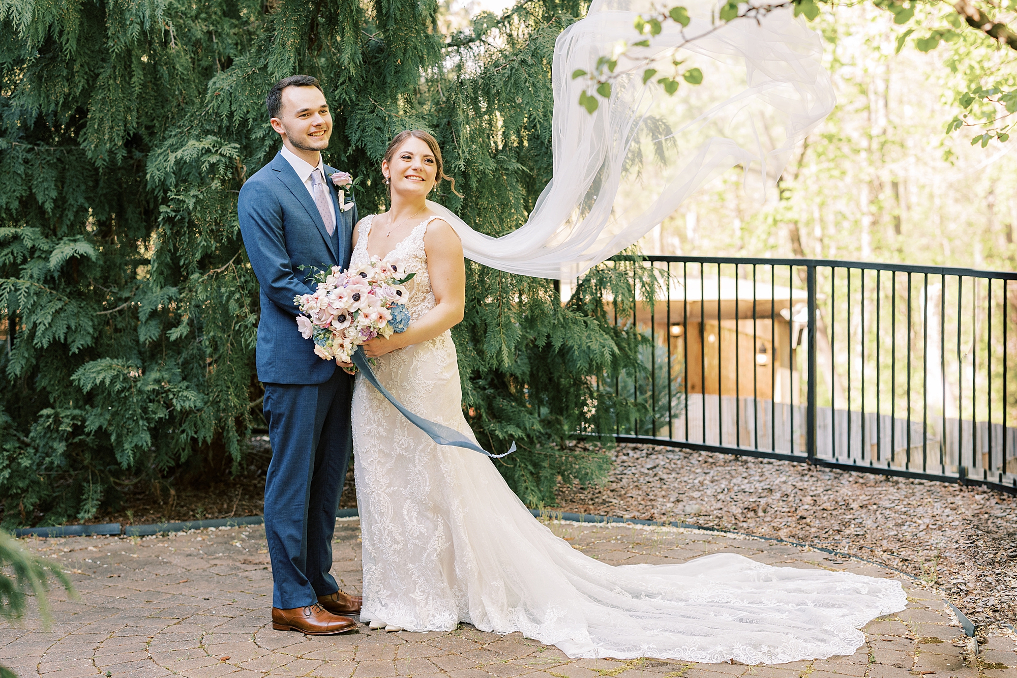 bride and groom smile with bride's veil floating behind them 