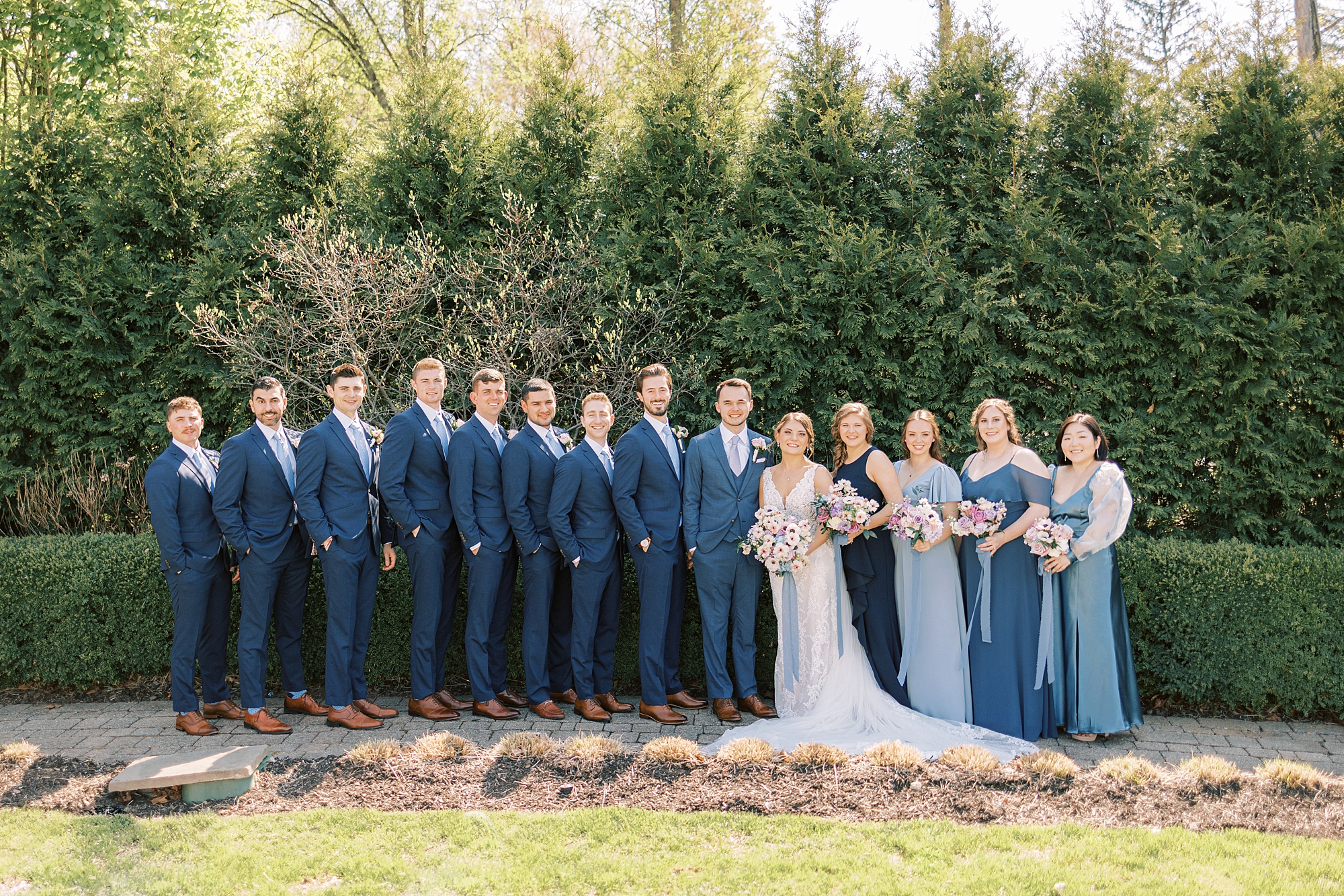 bride and groom stand with wedding party in blue suits and mismatched blue gowns