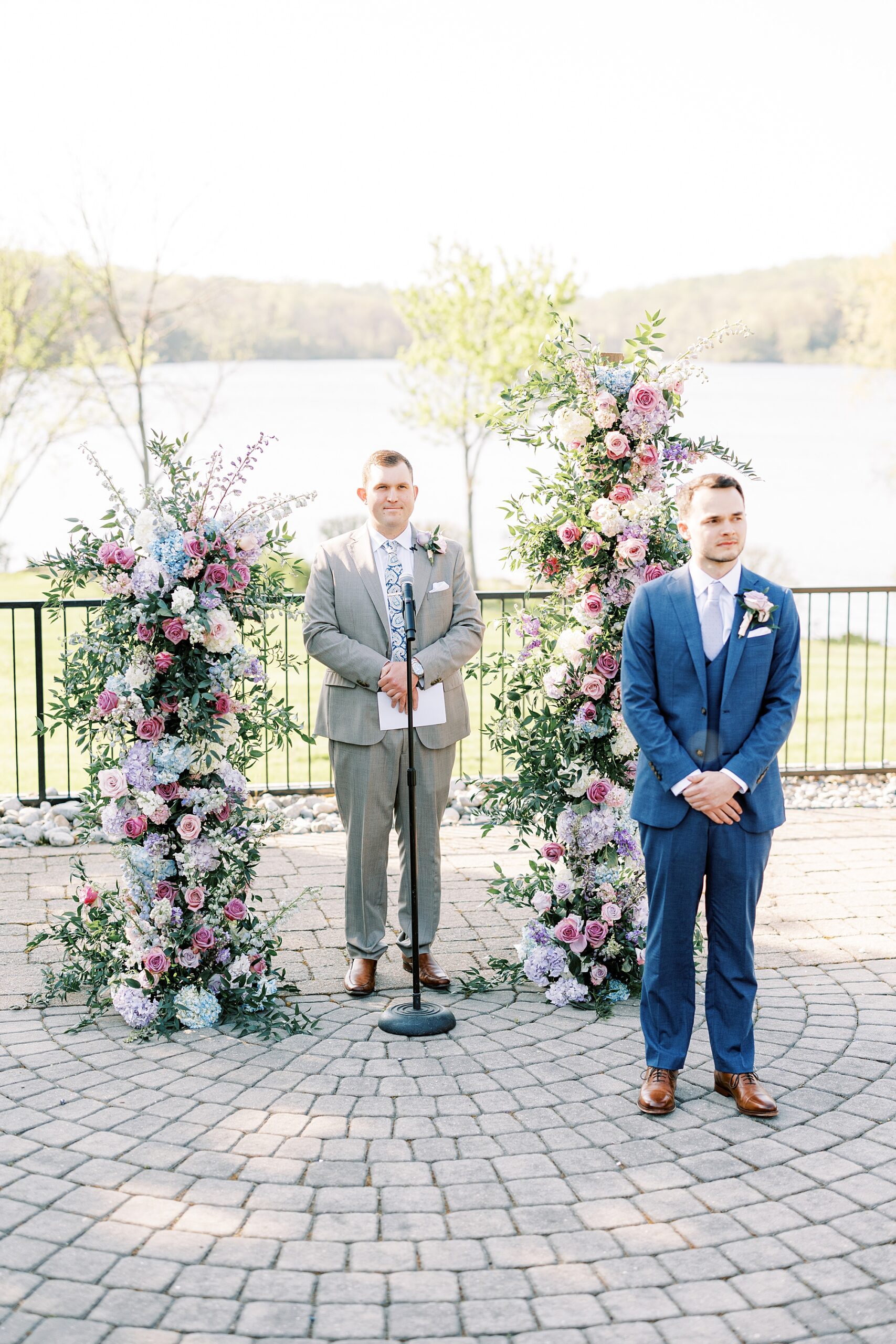 groom waits at altar bride before ceremony in the gardens at Lake House Inn with pink and purple flower installation