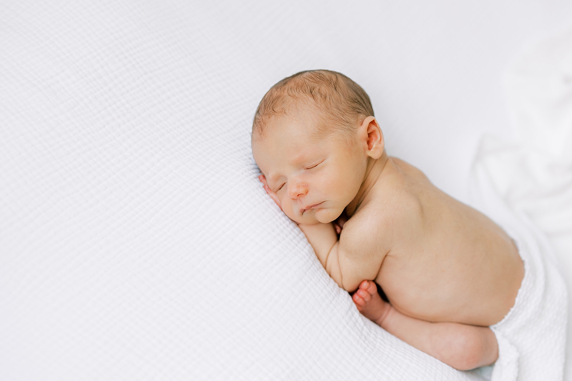 baby lays with white wrap on back during studio newborn photos in Media PA