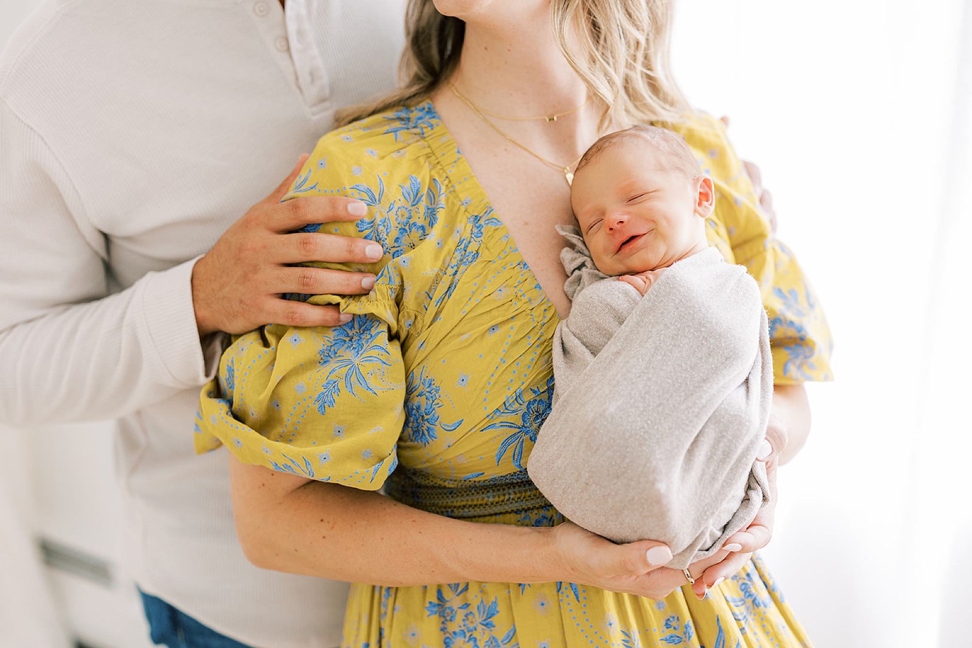 baby lays in white wrap against mom's chest in her yellow and blue floral dress 