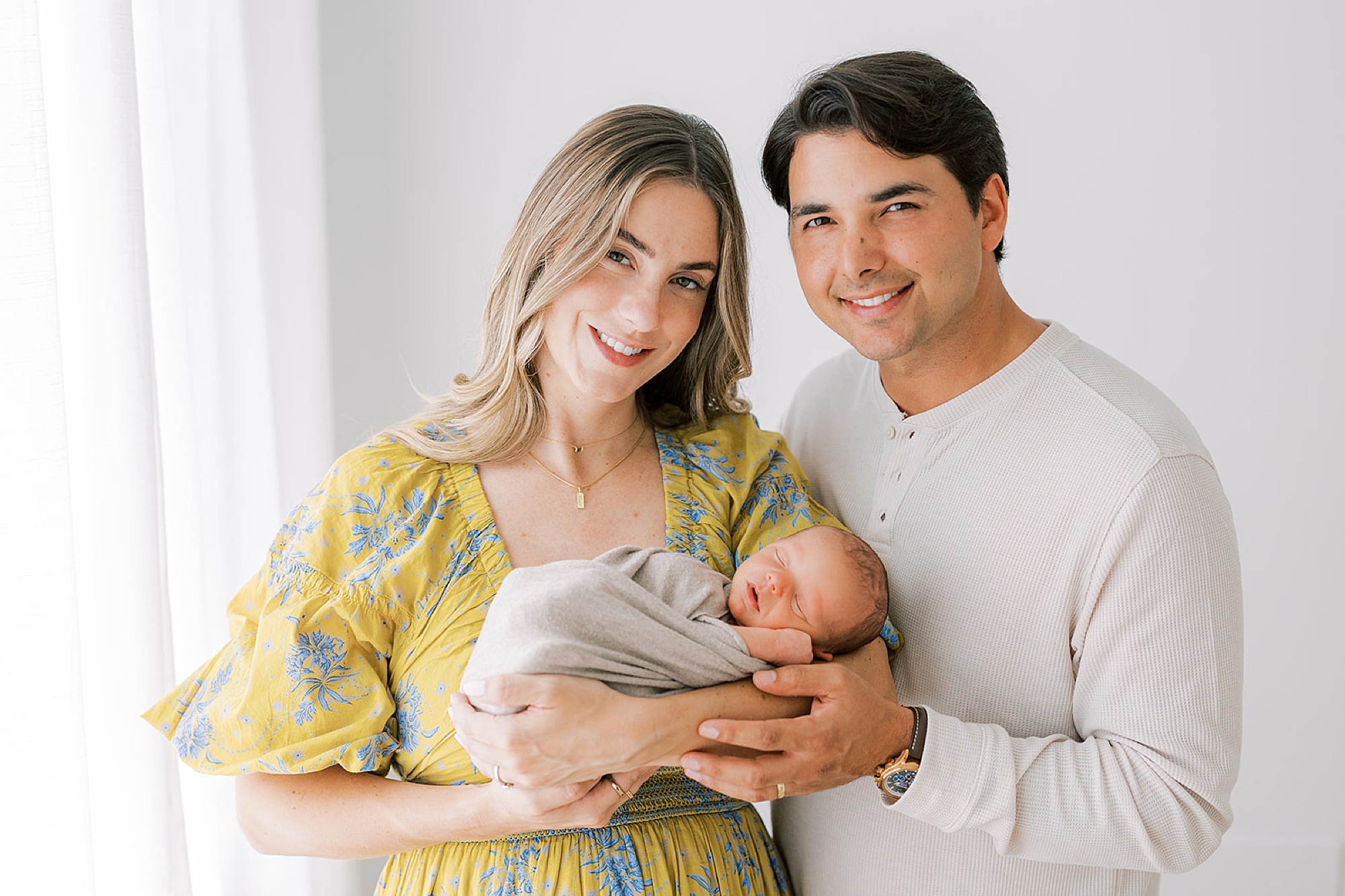 new parents stand smiling holding new son in mom's arms