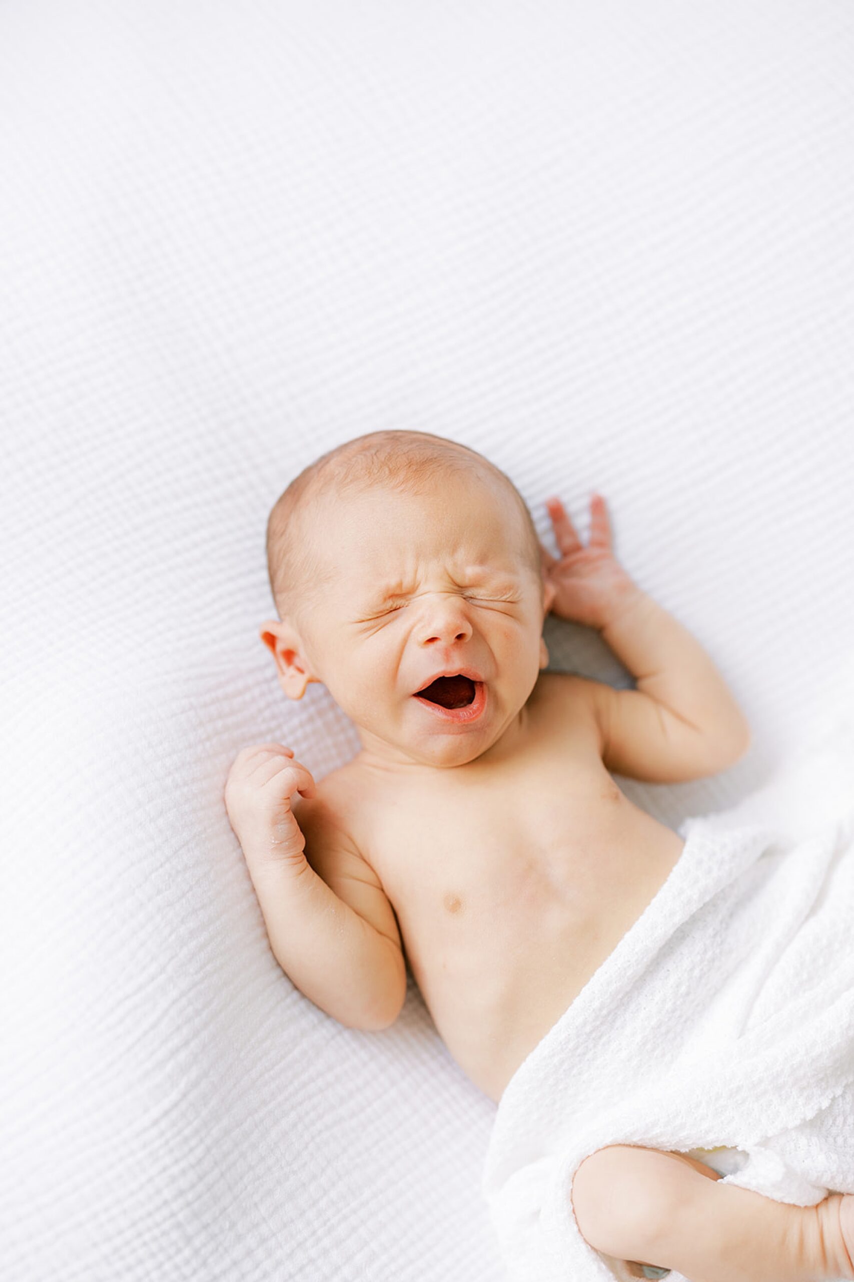 baby yawns during newborn photos in white blanket 