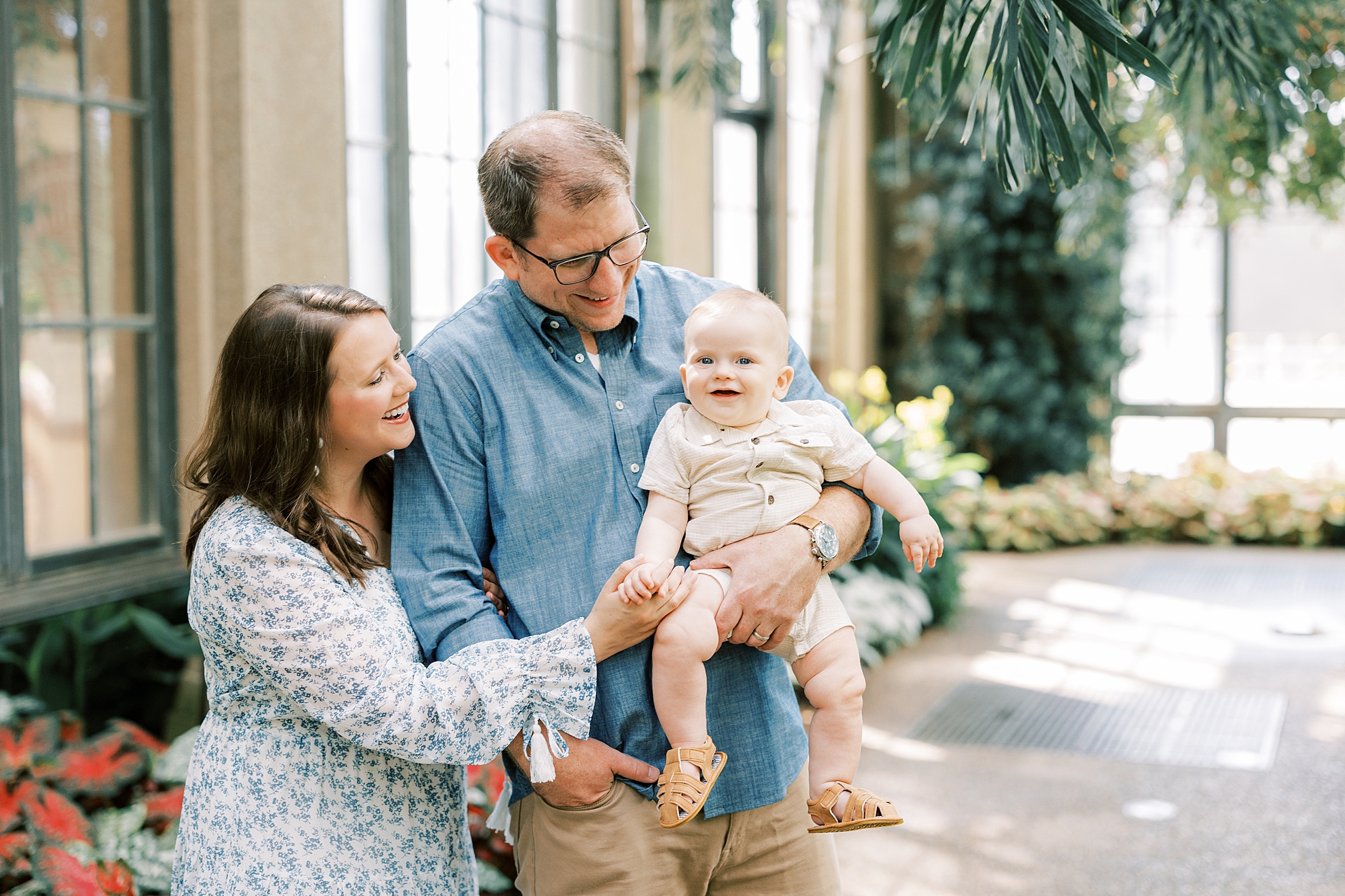 parents smile at son in dad's arms during portraits inside Longwood Gardens