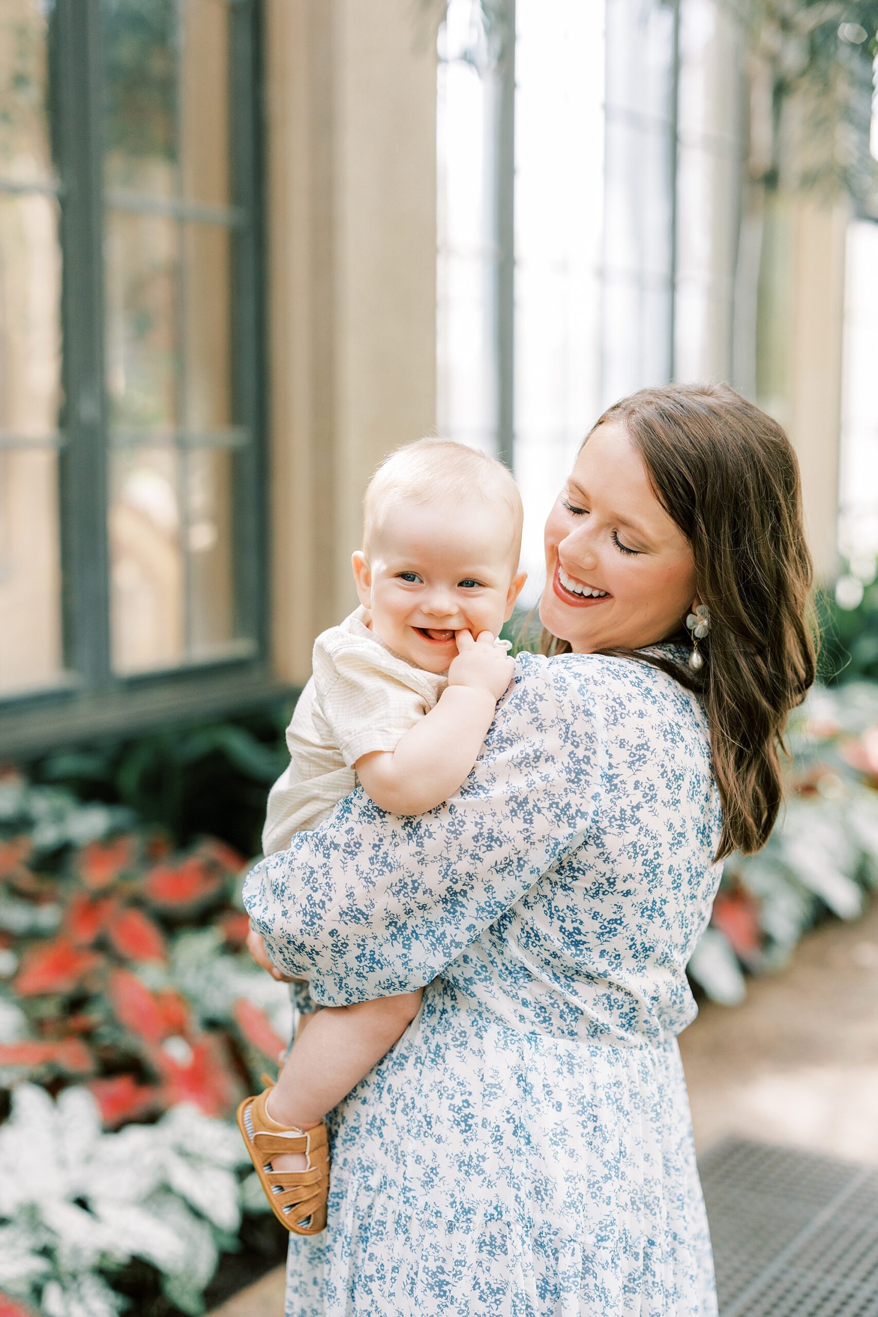 mom in flower dress holds son over shoulder laughing with him 