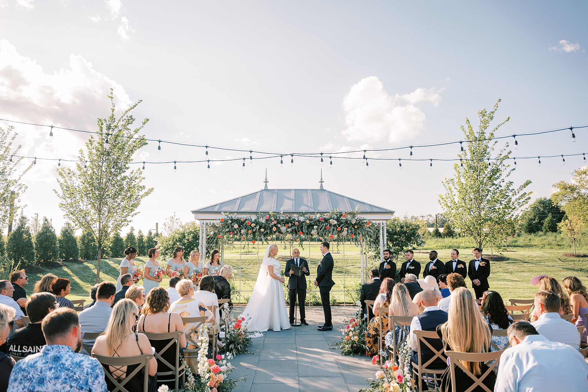 bride and groom hold hands exchanging vows under blue sky in gazebo 