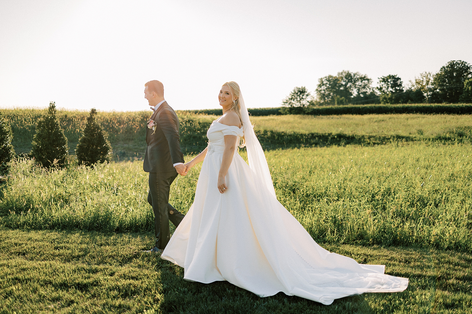 groom walks ahead of bride leading her along edge of field at Terrain Del-Val