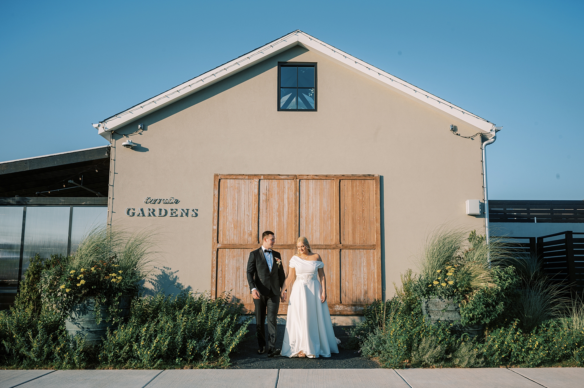 bride and groom hold hands in front of barn at Terrain Del-Val