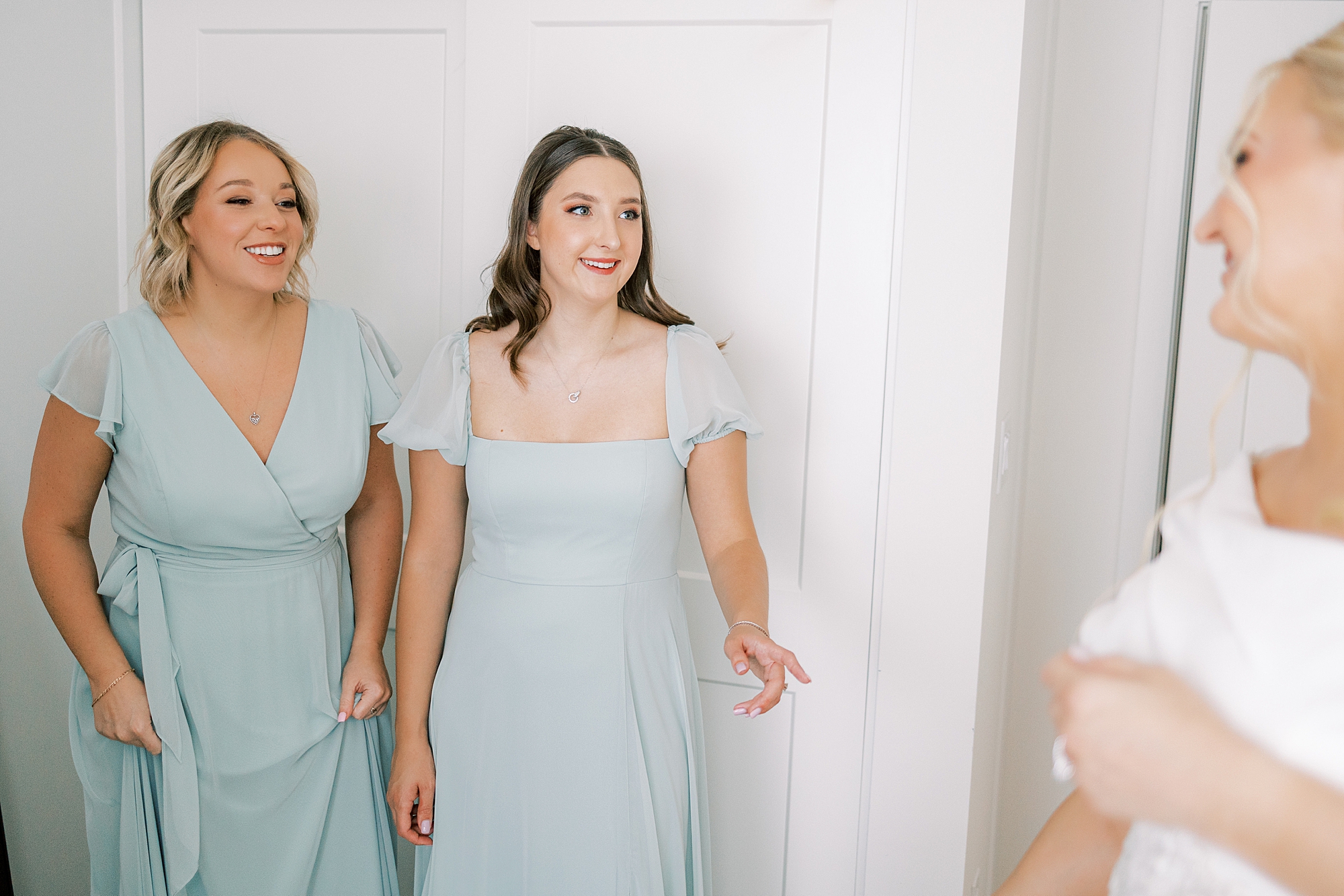 bridesmaids smile at bride looking at wedding gown for first time
