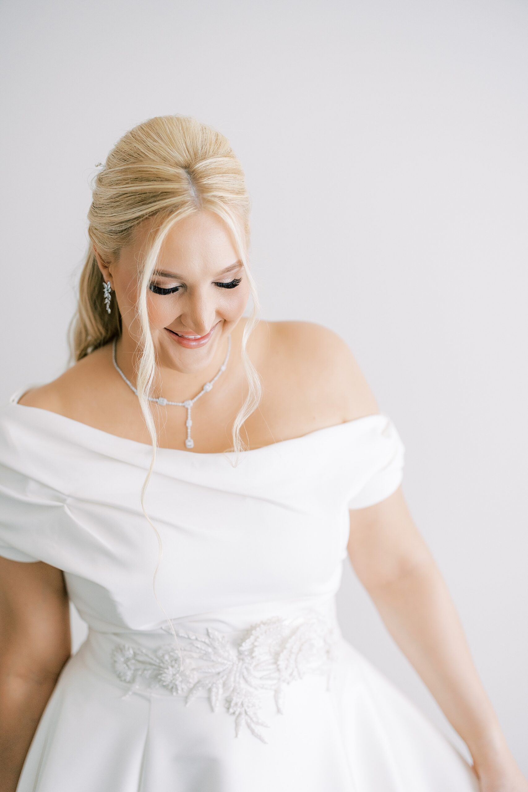 blonde bride smiles in off-the-shoulder wedding gown