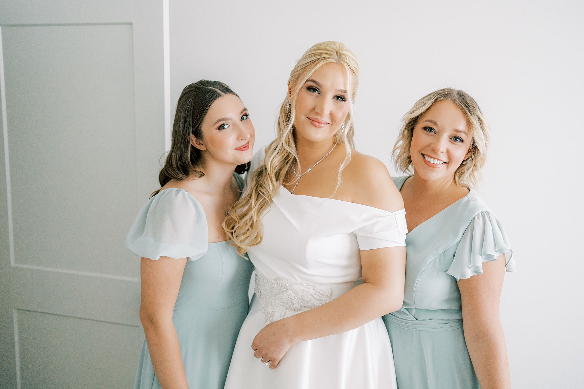 bridesmaids in blue gowns smile with bride in off-the-shoulder wedding gown