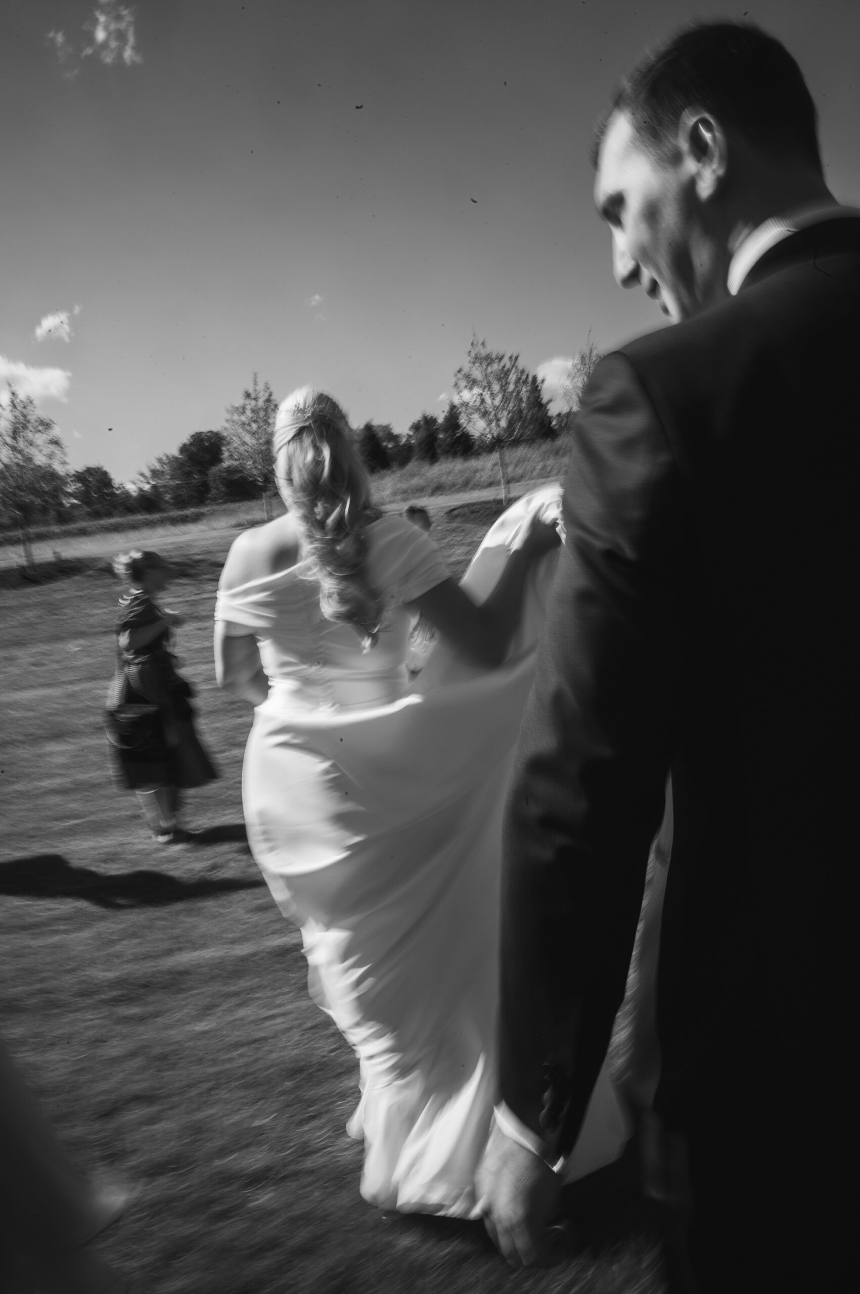 groom holds up bride's skirt walking through field for photos 