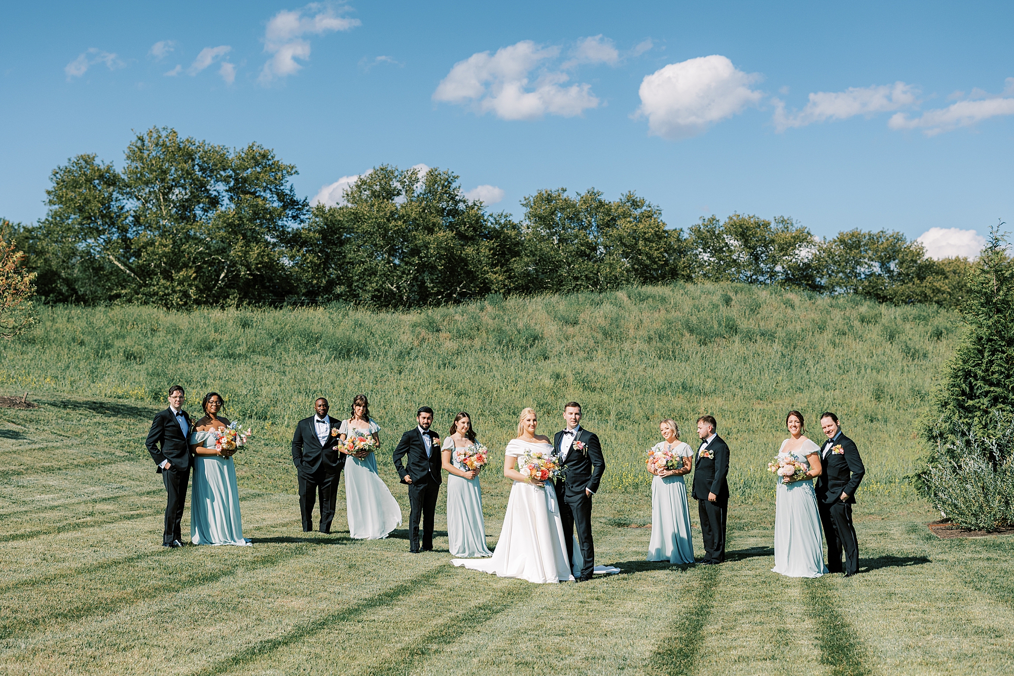 bride and groom stand in field at Terrain DelVal with wedding party around them 