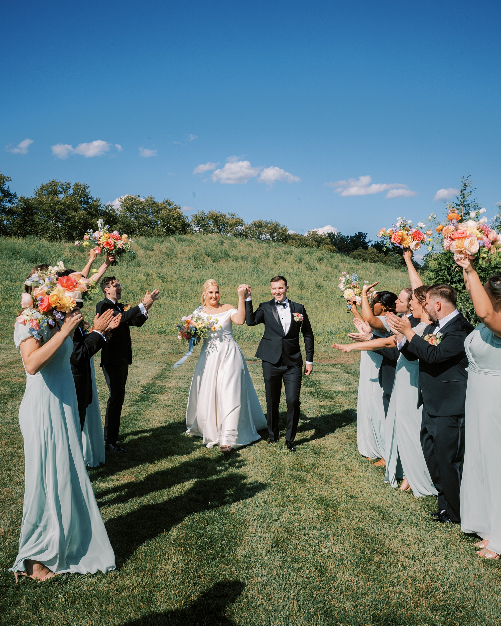 bridal party cheers lifting up bouquets while newlyweds walk through at Terrain DelVal