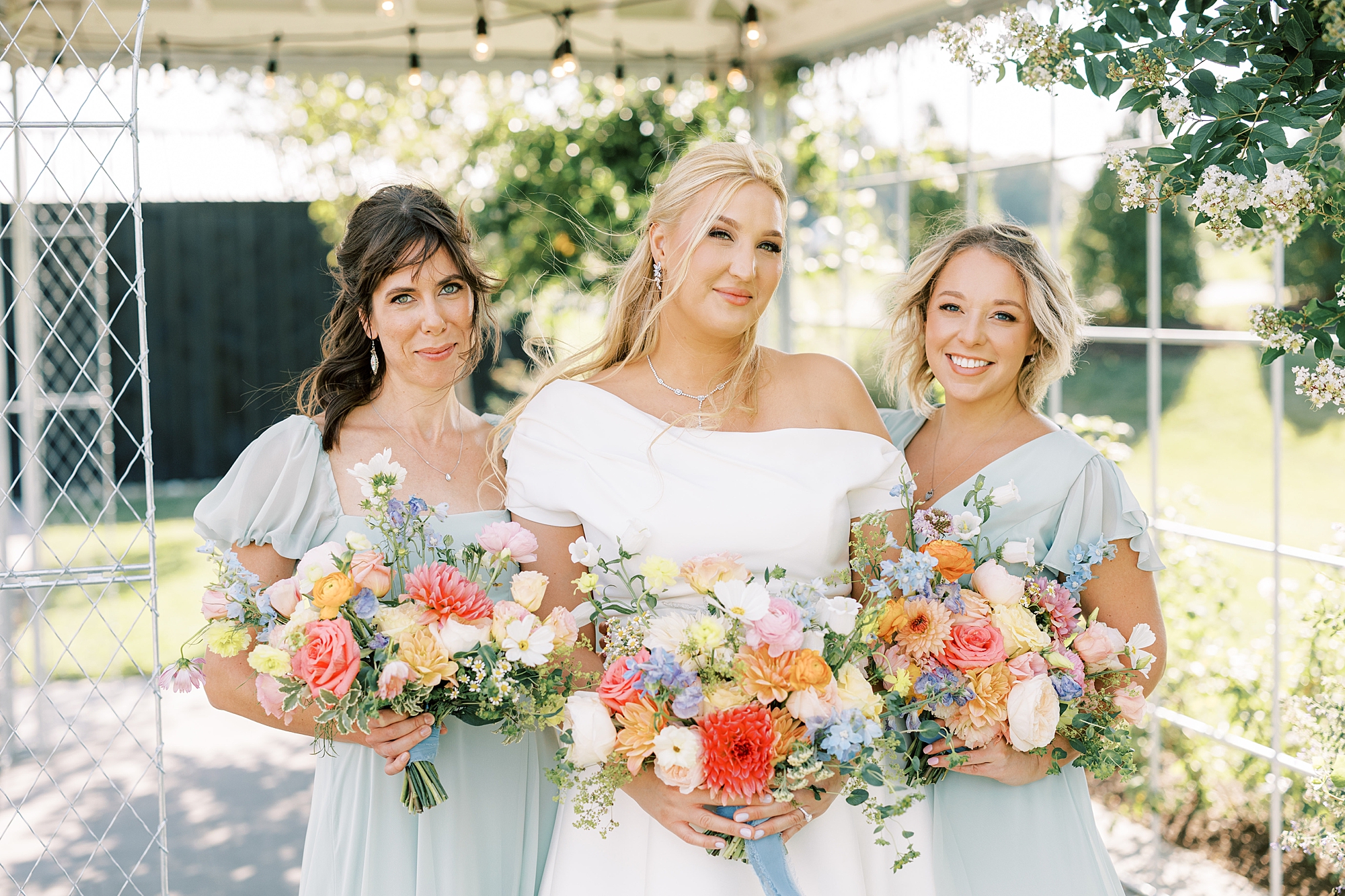 bride stands with bridesmaids in light blue gowns with bright colored bouquets 