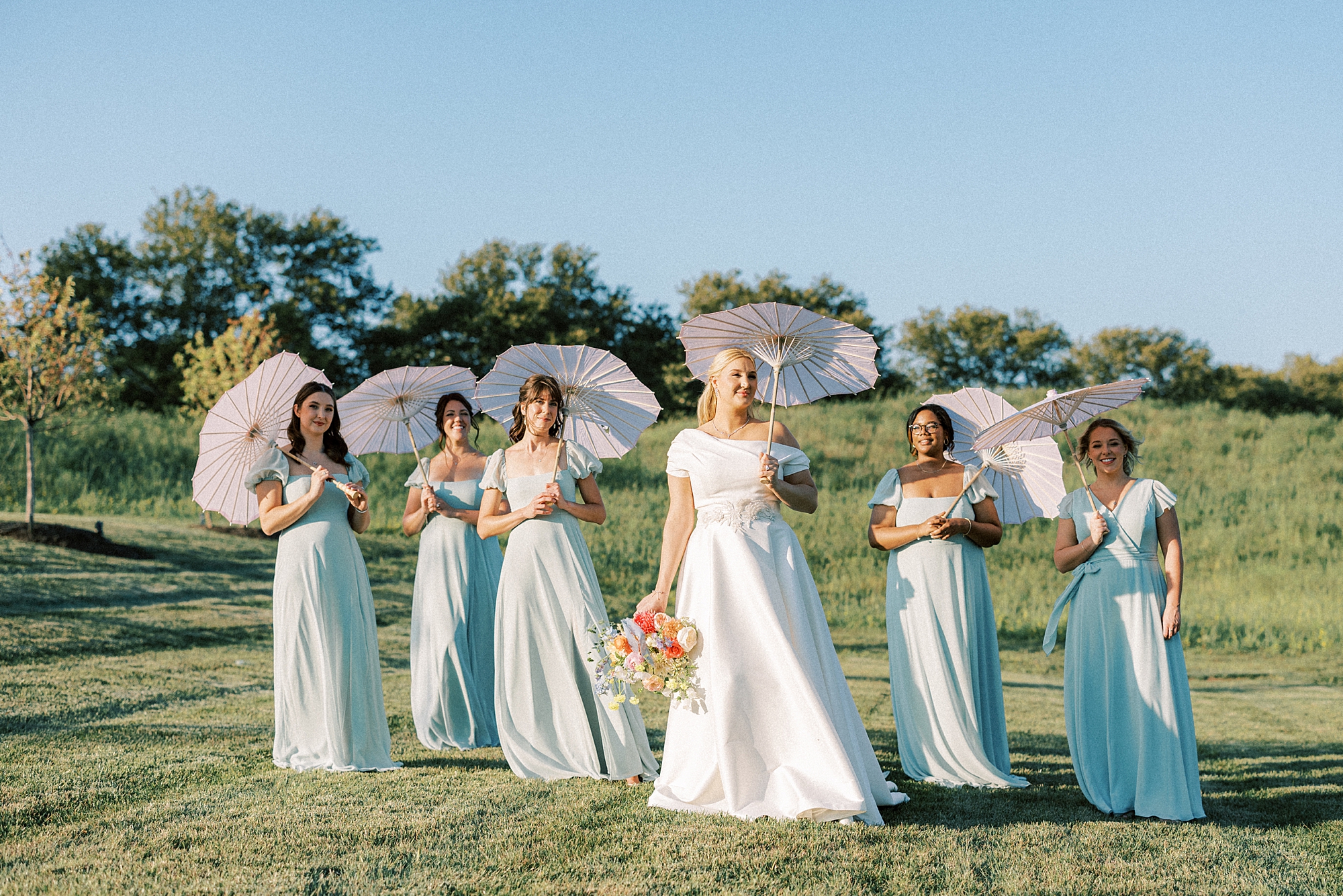 bride stands with bridesmaids under parasols on hill at Terrain DelVal