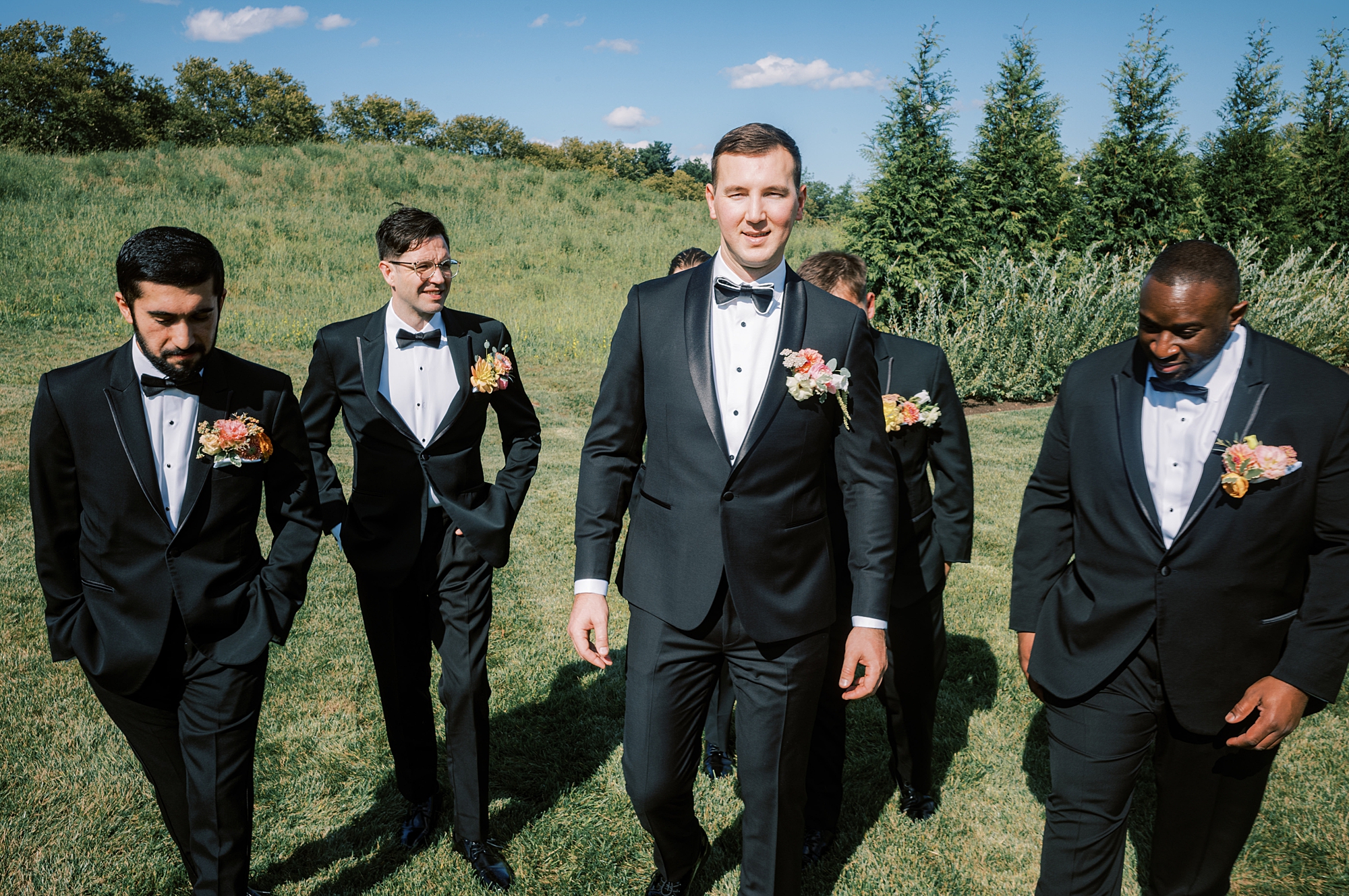 groom and groomsmen in black suits walk along hill at Terrain DelVal