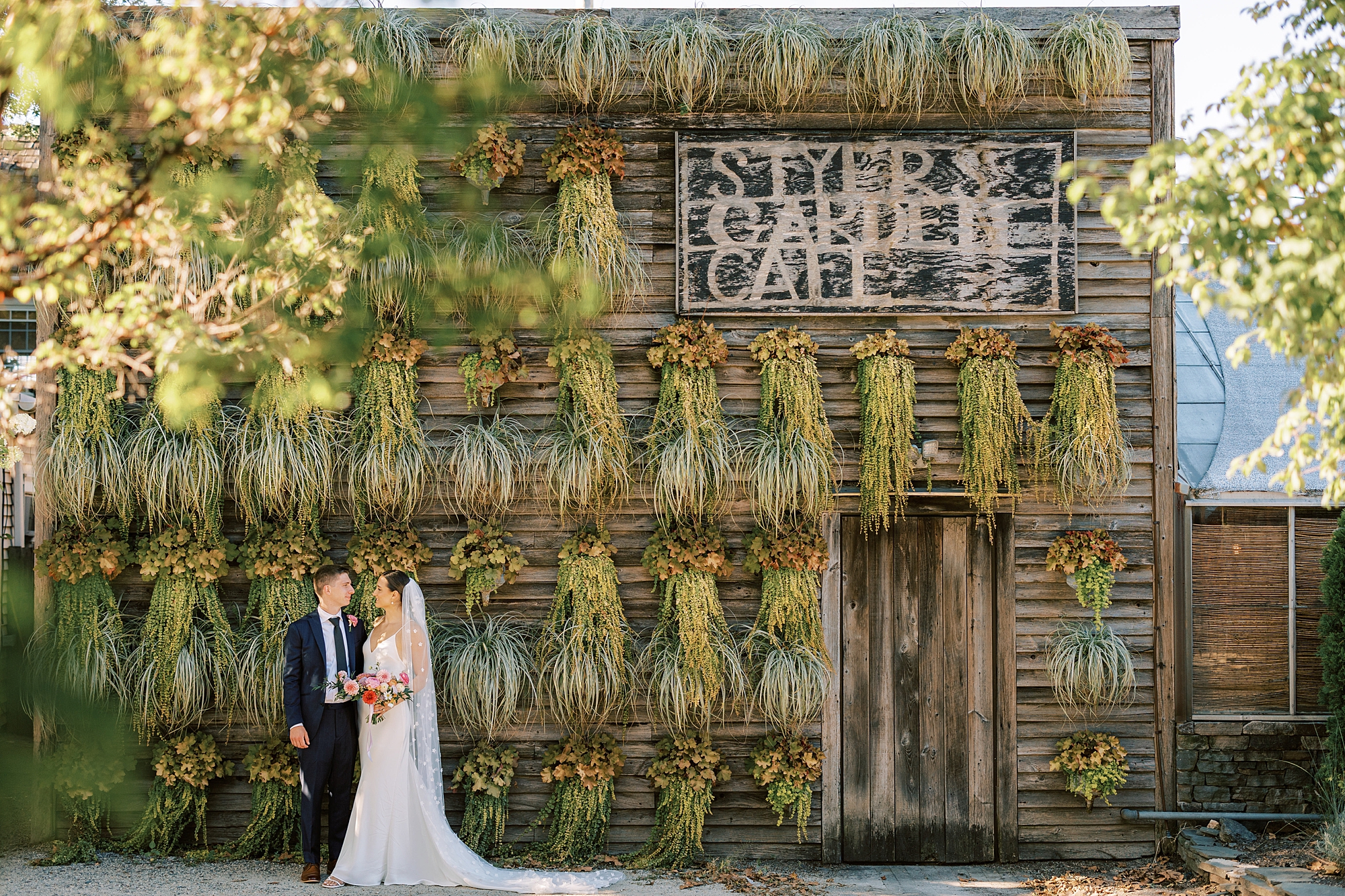 bride and groom hug near greenery covered wall at the Terrain at Styer's in Glen Mills PA