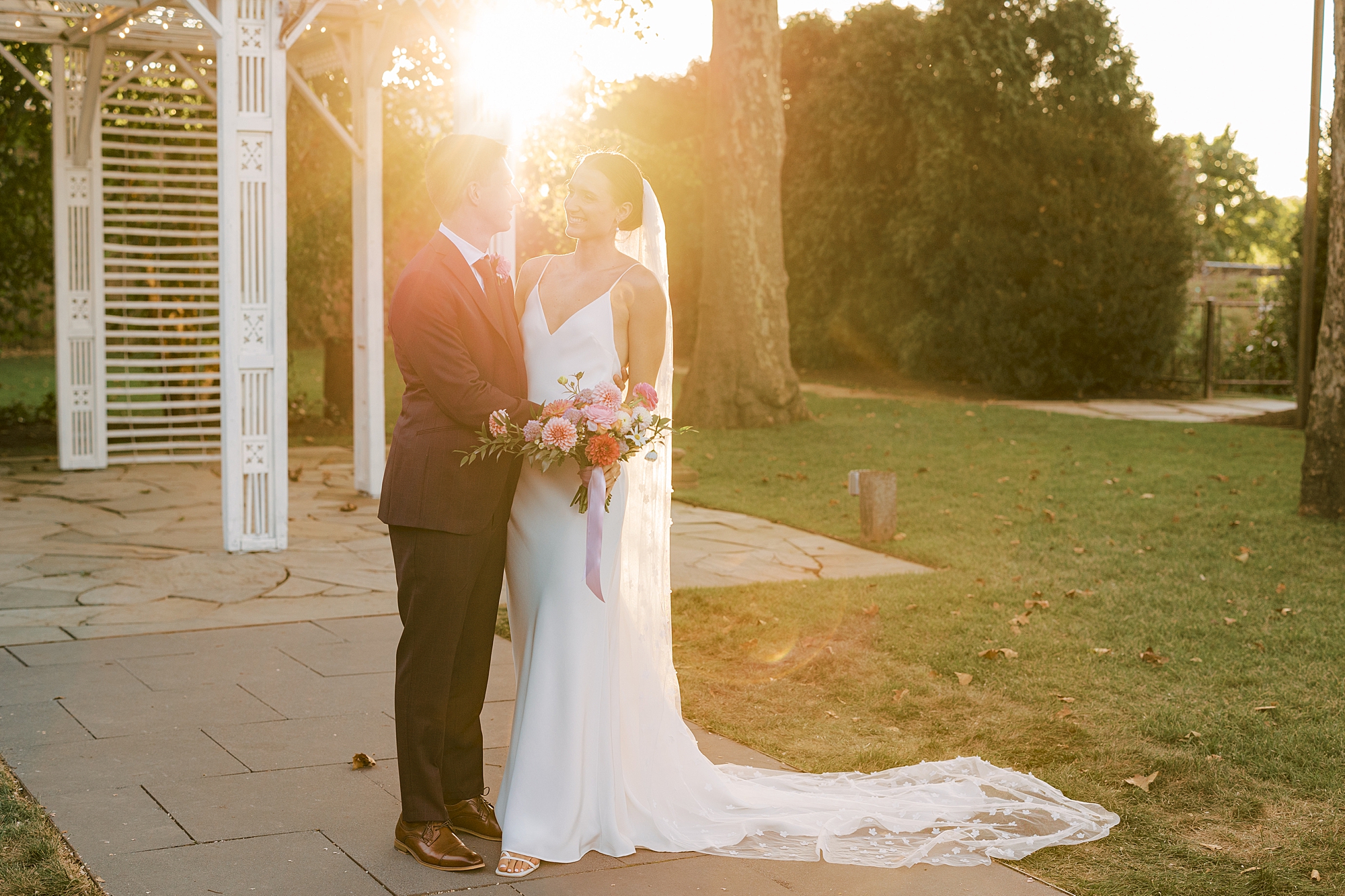 bride and groom hug in front of white gazebo at sunset inside the Terrain at Styer's