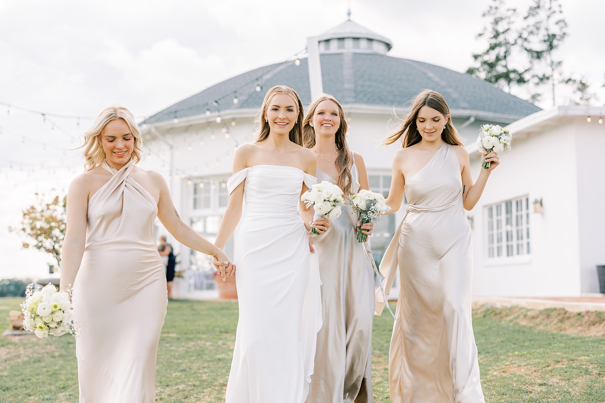 bride walks with bridesmaids in light champagne gowns outside the Rotunda at Lauxmont Farms 