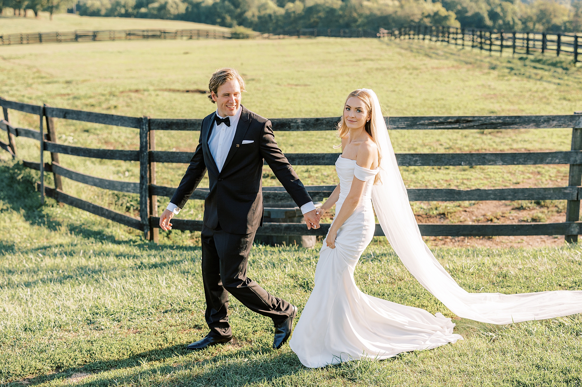 bride grins walking with groom along wooden fence at Lauxmont Farms