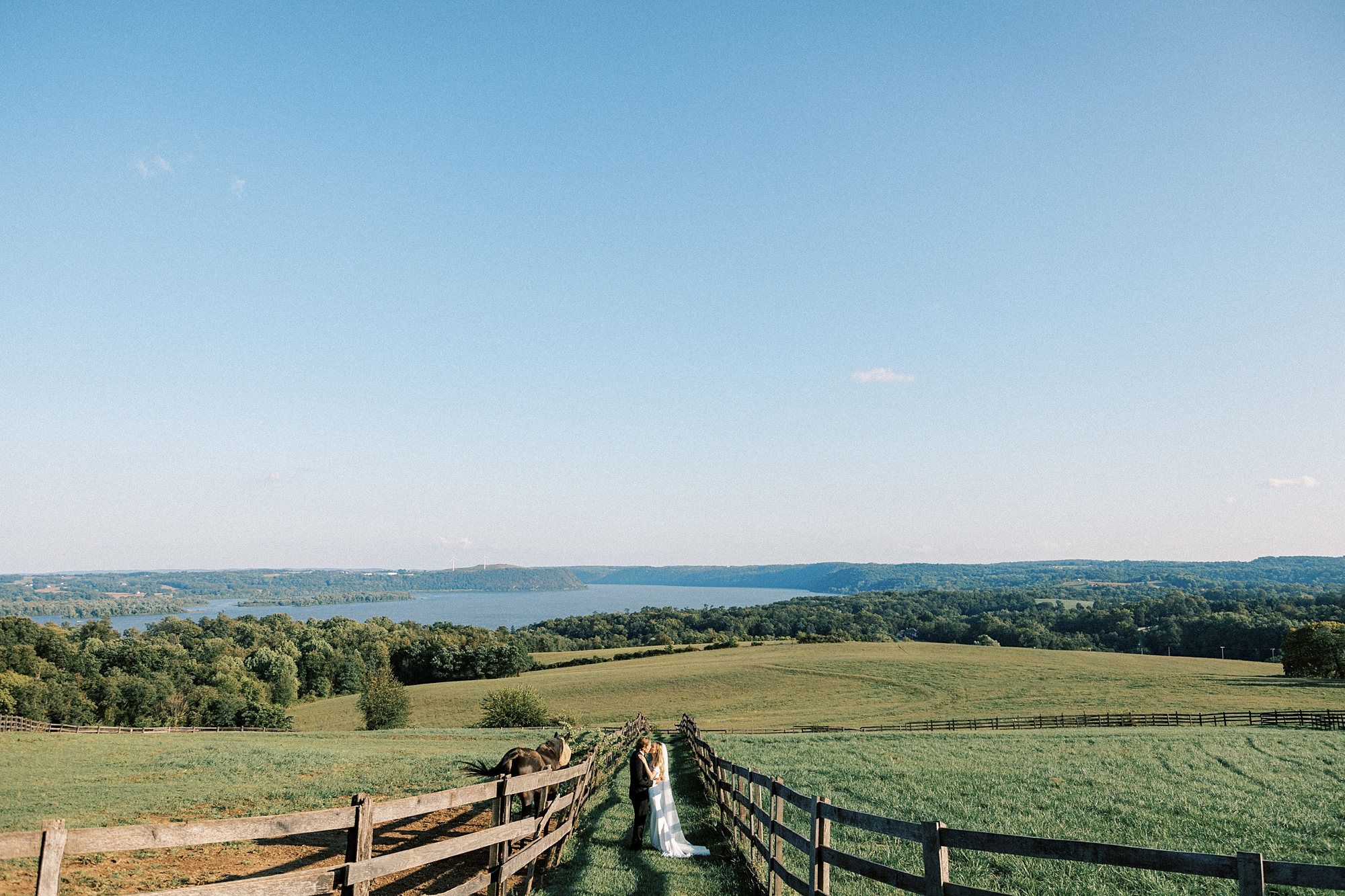 newlyweds hug between fences with big sky above them 