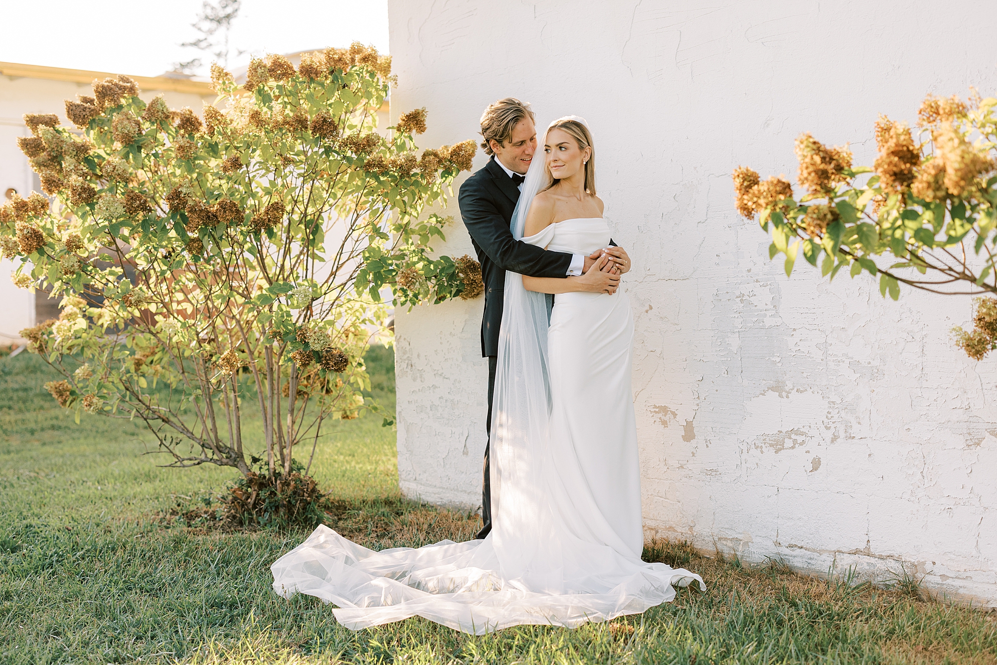 bride and groom hug along white wall at Lauxmont Farms