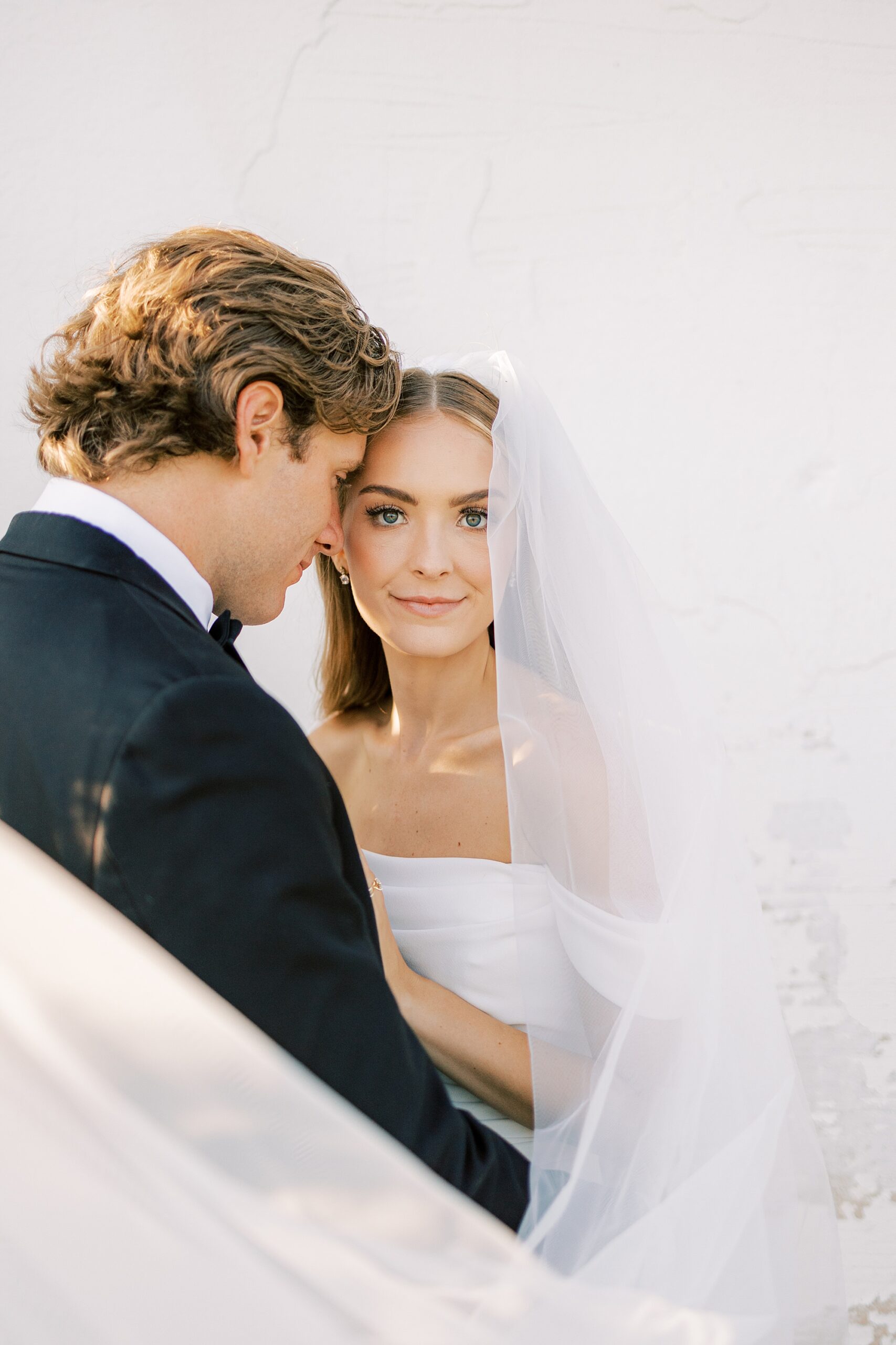 groom leans into bride with veil around them in the summer