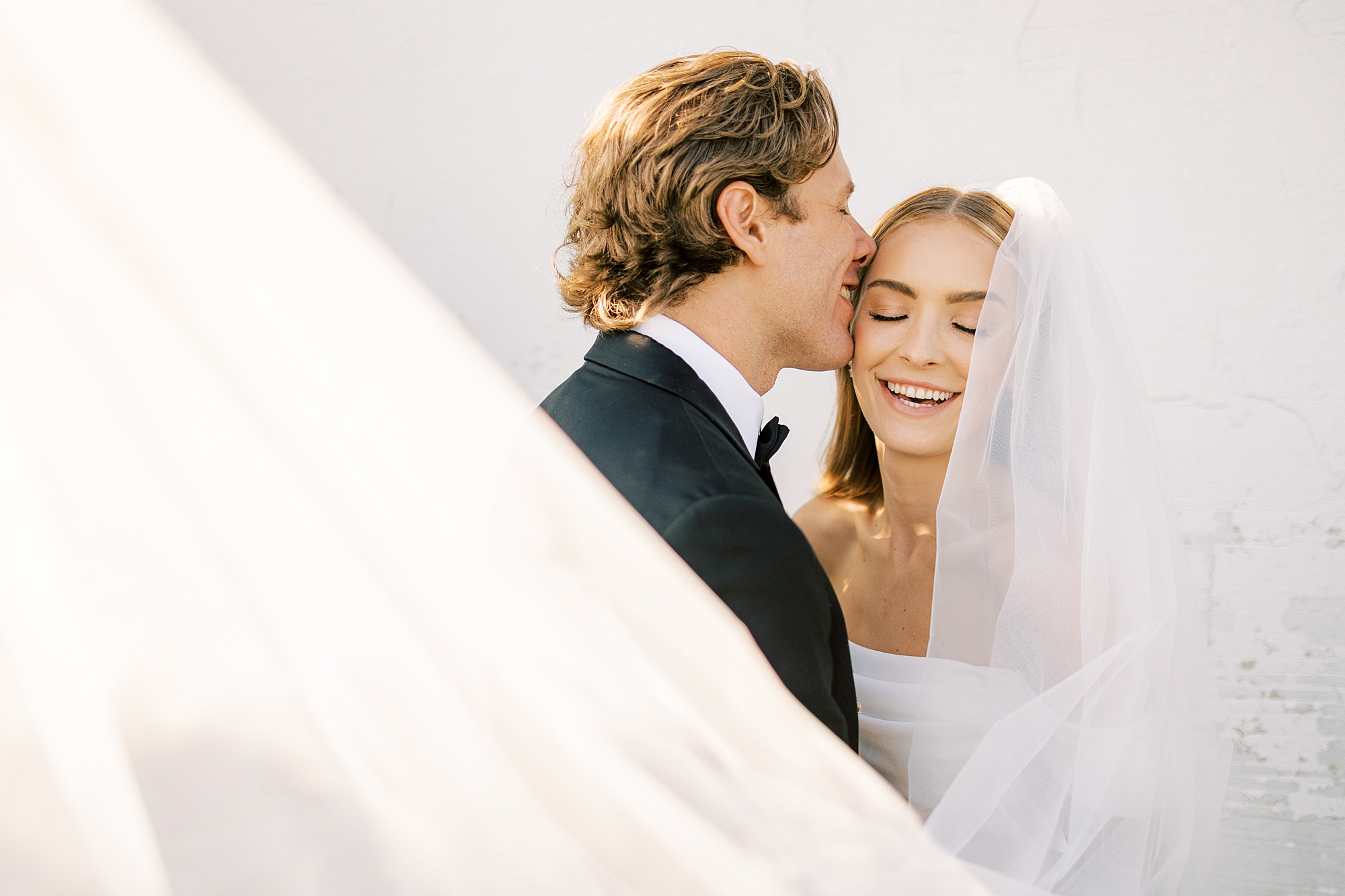 groom hugs bride and kisses her forehead during summer wedding