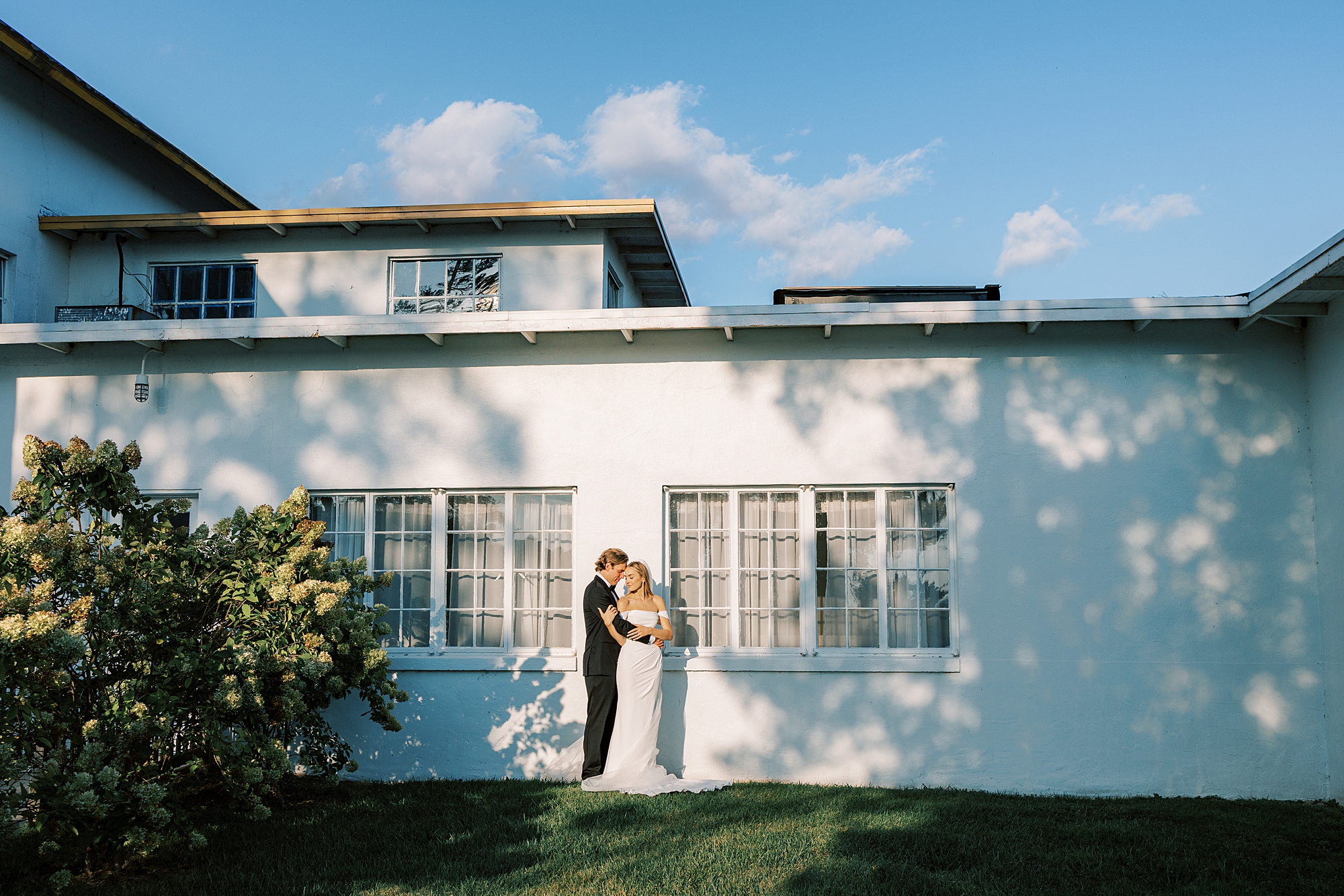 bride and groom hug in shadows along white wall of Rotunda at Lauxmont Farms