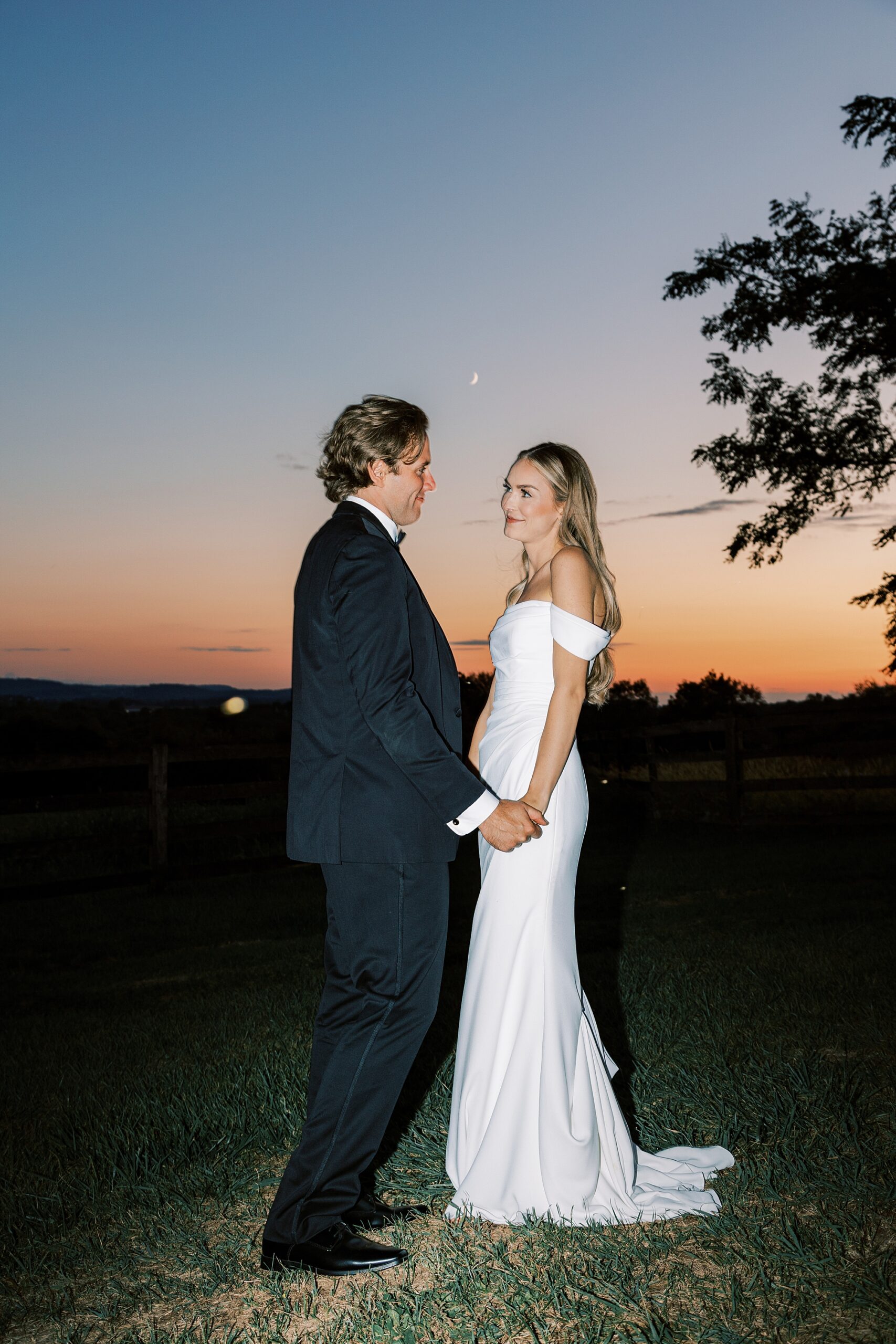 bride and groom hold hands as sunsets on hill at Lauxmont Farms