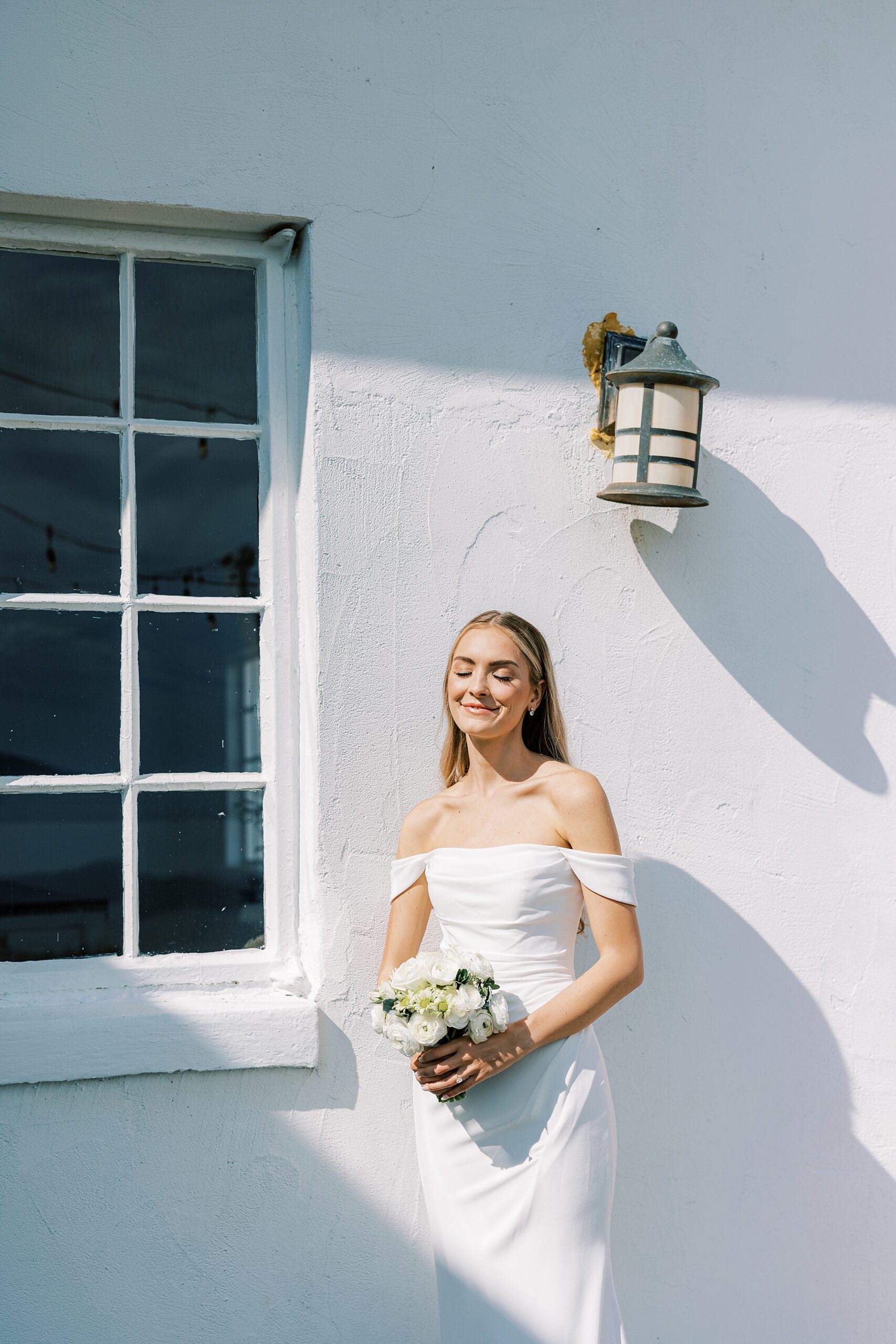 bride smiles leaning against white wall in shadows at Lauxmont Farms