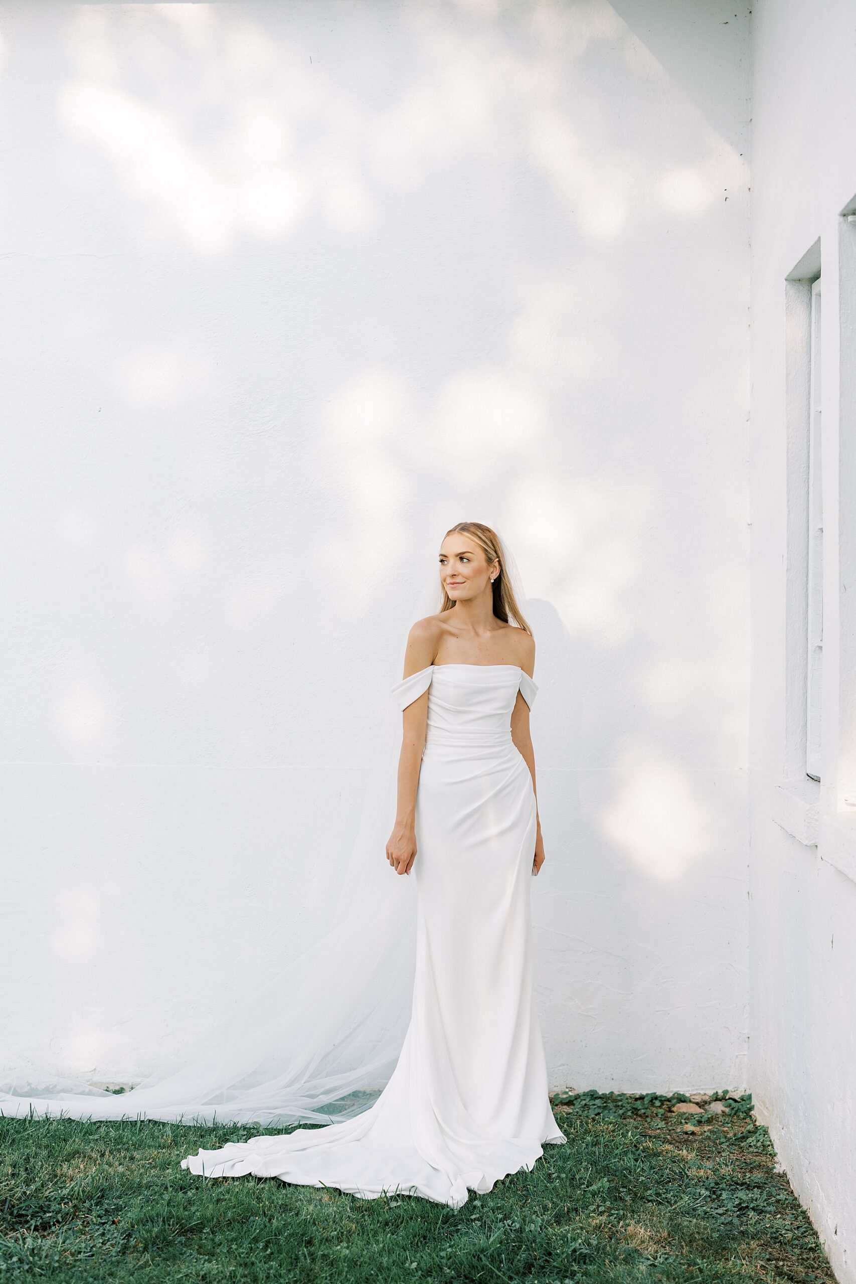 bride leans against white wall of Lauxmont Farms