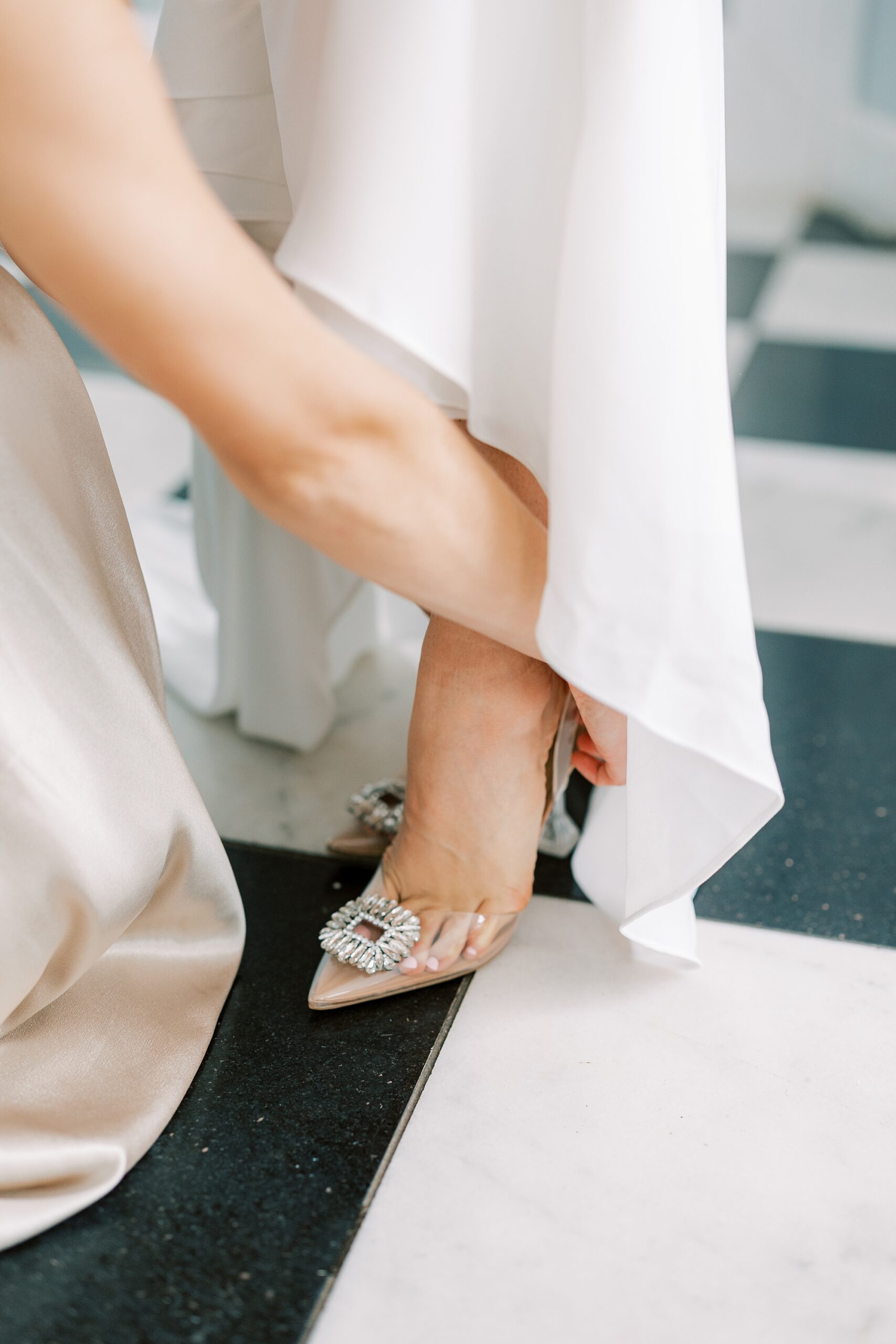 bridesmaid helps bride into wedding shoes 