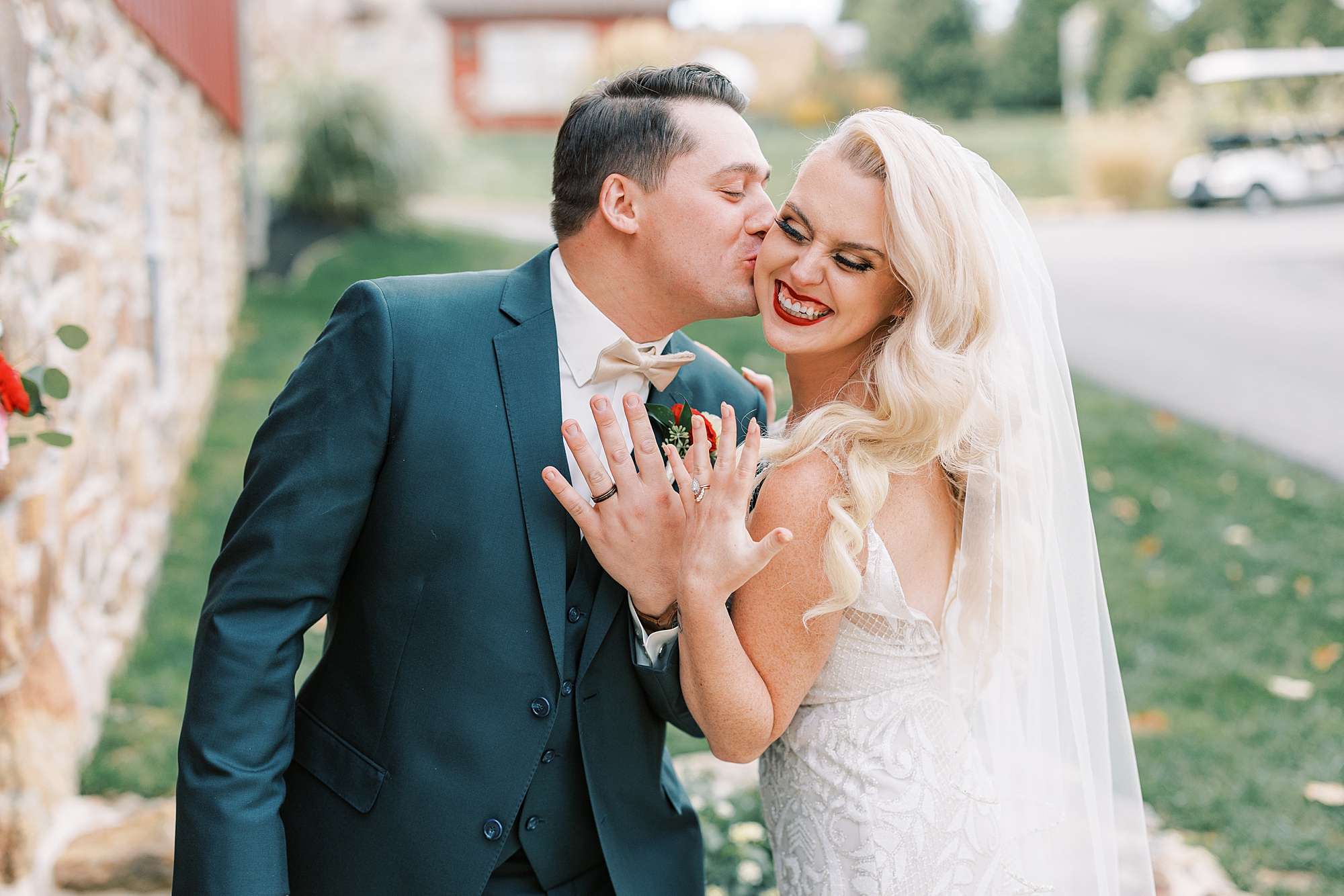 groom leans to kiss bride's cheek while they hold up wedding rings