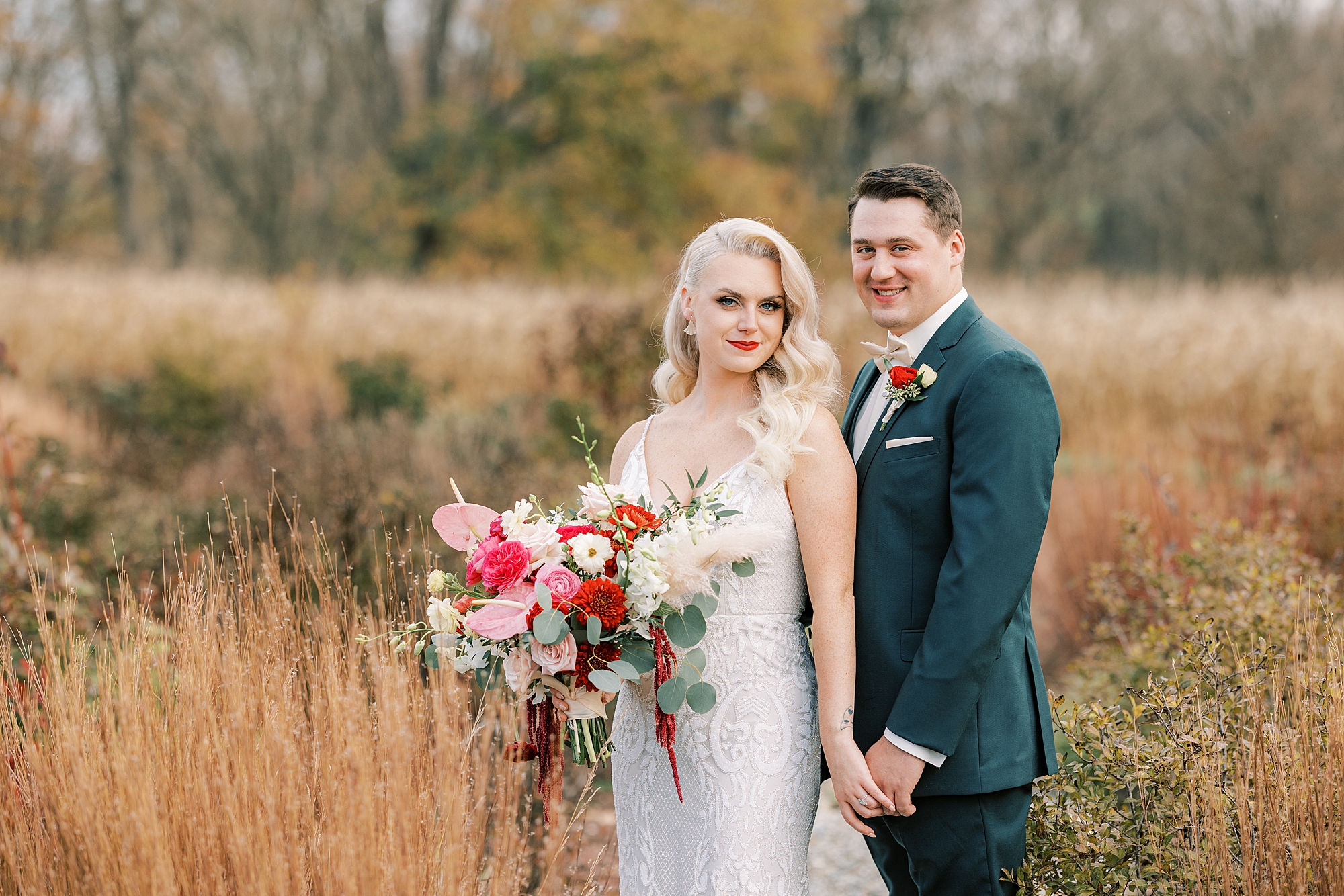 groom holds mom's hand in front of chest while she holds bouquet of pink flowers 