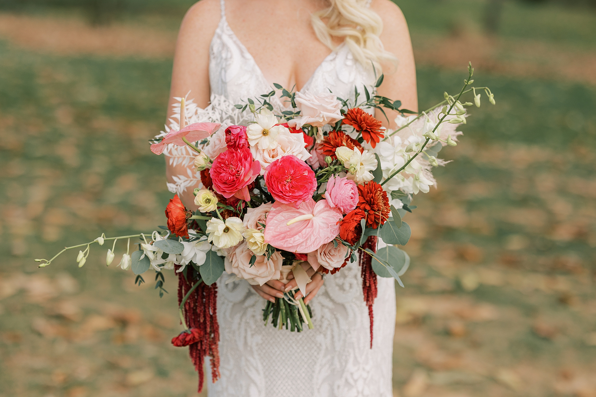 bride holds bouquet of pink, red, and white flowers for fall wedding day